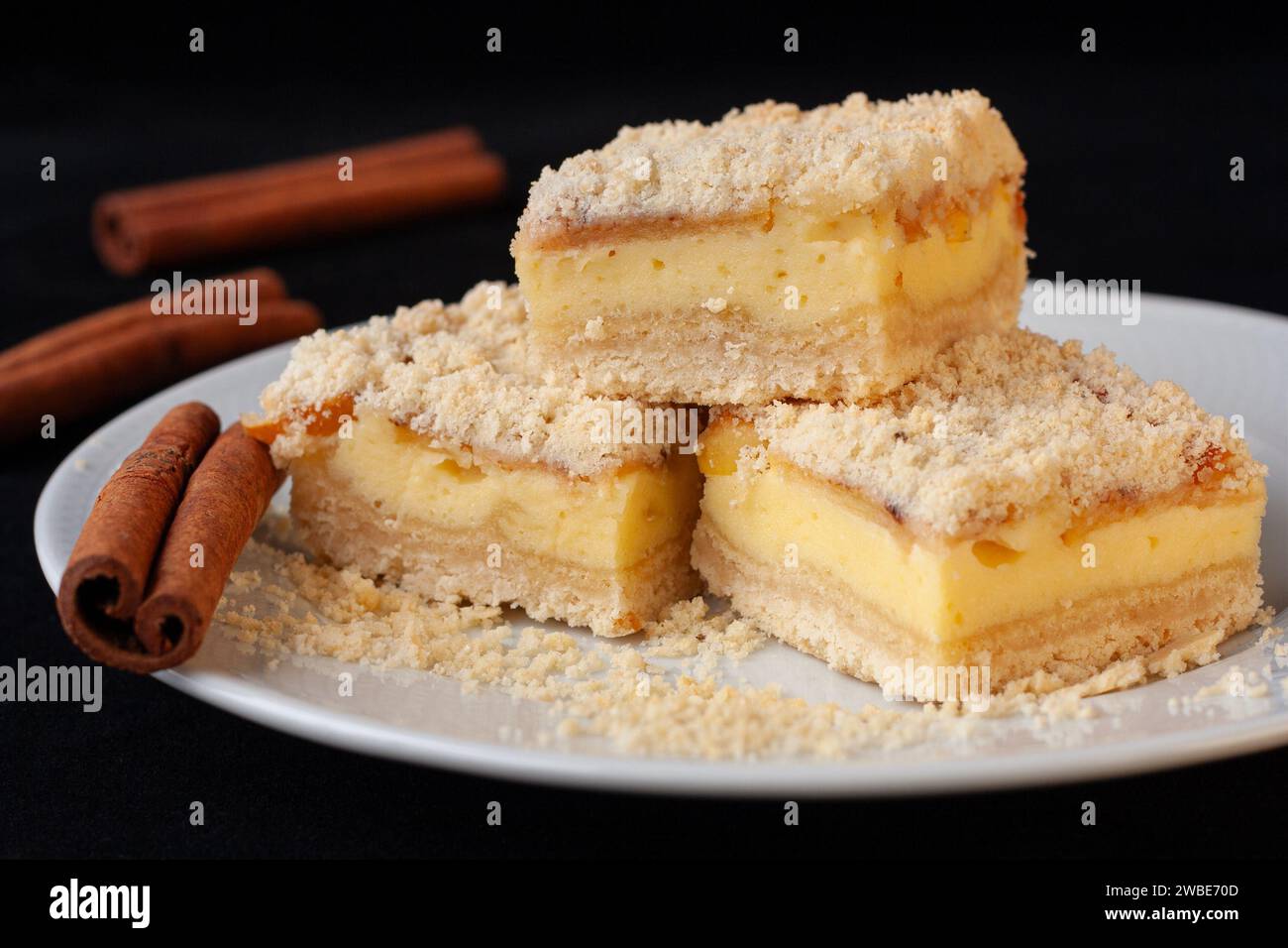Torta di mele a fette fatta con pasta frolla con crema di formaggio cottage e spicchi di mele su un piatto bianco su sfondo nero. bastoncini di cannella Foto Stock