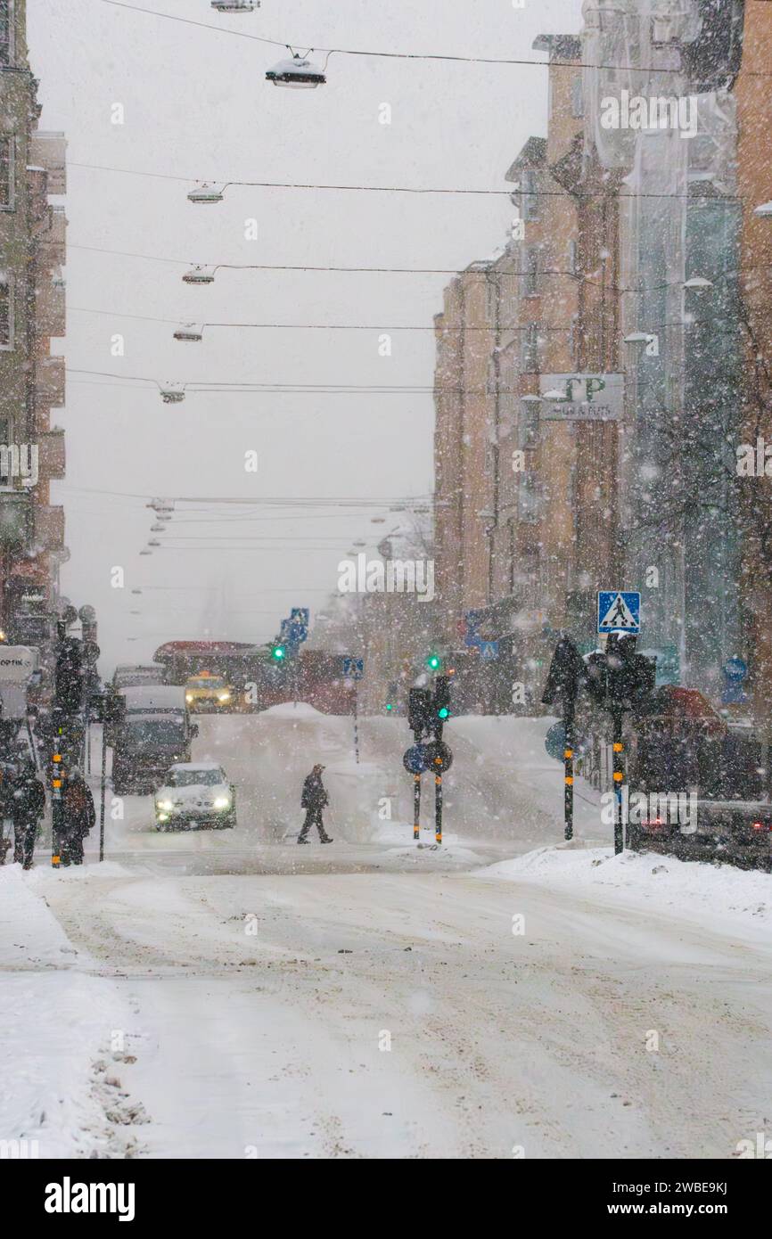 Una strada di Stoccolma, Svezia (renstiernas gata) durante una tempesta di neve invernale, persone che camminano, auto che guidano e neve sulla strada. Ventoso, bufera di neve Foto Stock