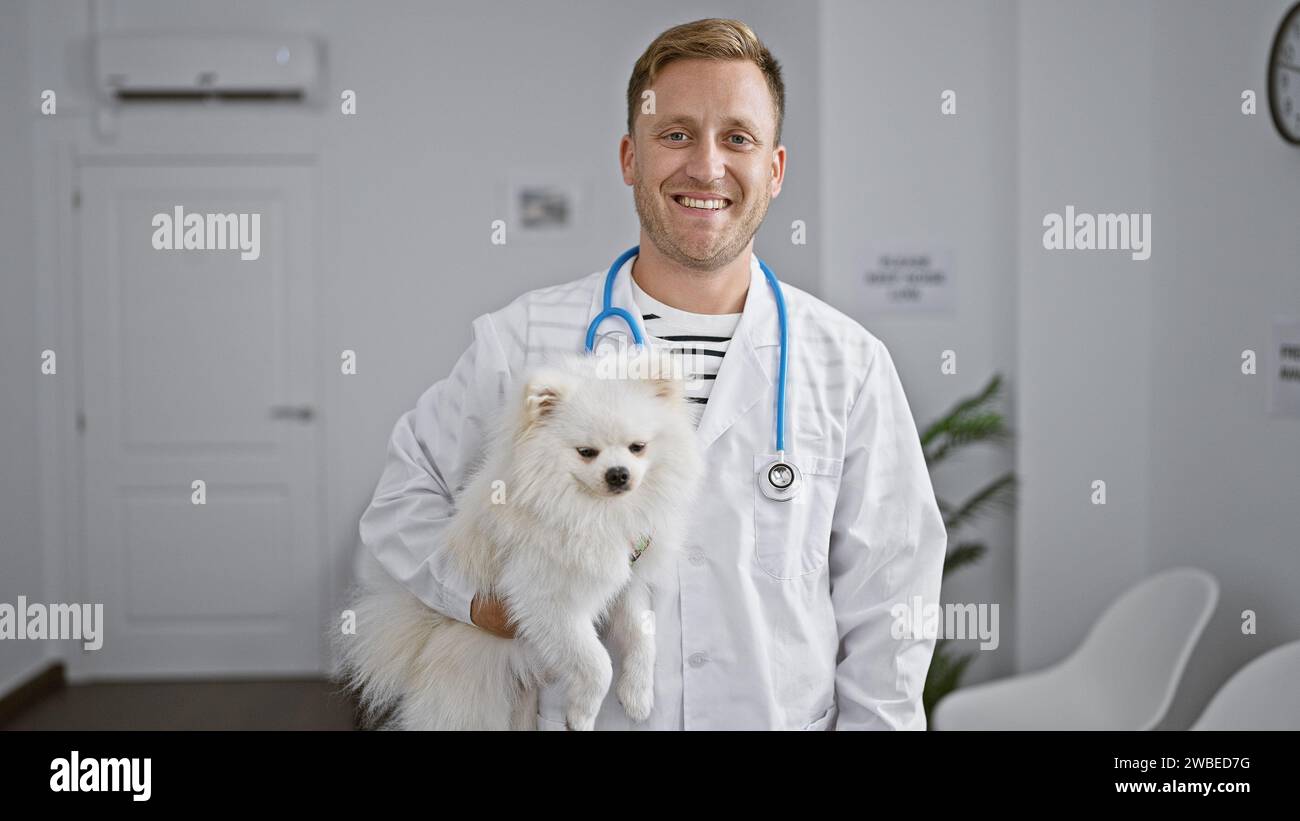 Giovane e sicuro uomo caucasico sorride mentre si trova con il suo carino cane alla clinica del veterinario, felice della diligente cura e dell'esame professionale di Foto Stock