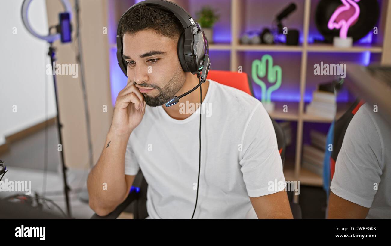 Un giovane concentrato con la barba che indossa cuffie e cuffie in una moderna sala giochi di notte. Foto Stock