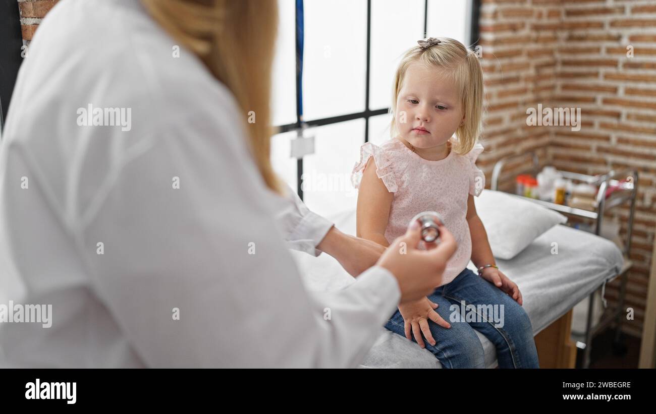 Pediatra premuroso in clinica esaminando il torace del paziente bambino adorabile utilizzando lo stetoscopio, garantendo respiro abbondante durante l'esame medico in accogliente guarigione interna Foto Stock