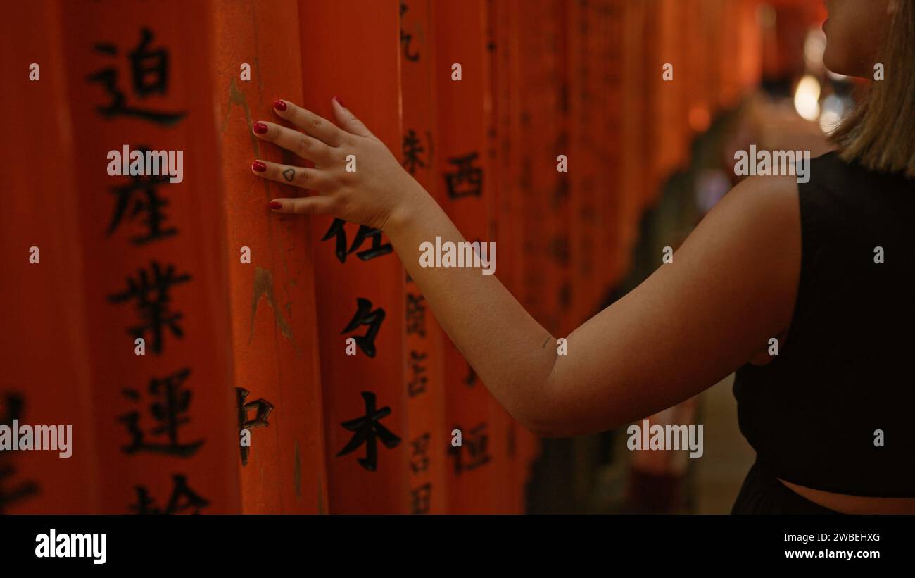 La riverente passeggiata della giovane donna, che cammina e tocca le tradizionali porte torii giapponesi a fushimi inari-taisha, uno sguardo all'indietro mentre si muove lungo il fiume Foto Stock