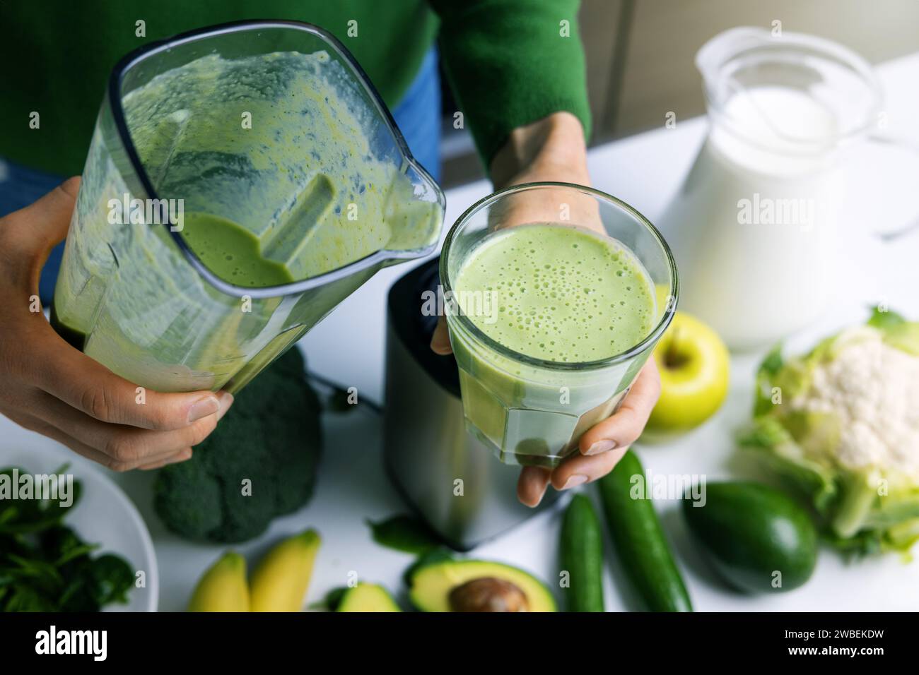 donna che versa frullato verde fresco fatto in casa in un bicchiere a base di frutta e verdura. stile di vita sano Foto Stock