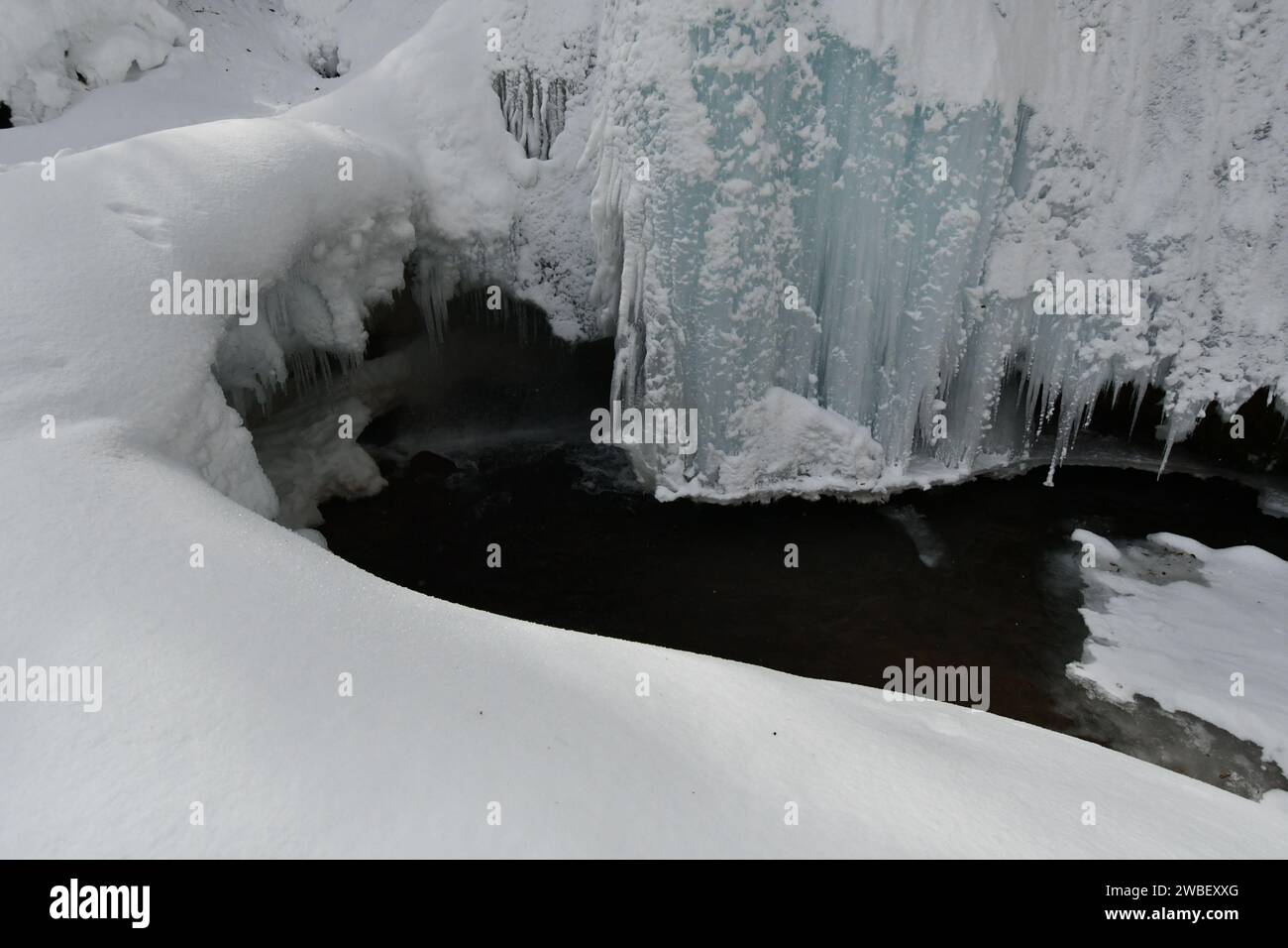 Un'idilliaca scena invernale con una serena cascata ghiacciata che scende su rocce e sculture di neve sullo sfondo Foto Stock