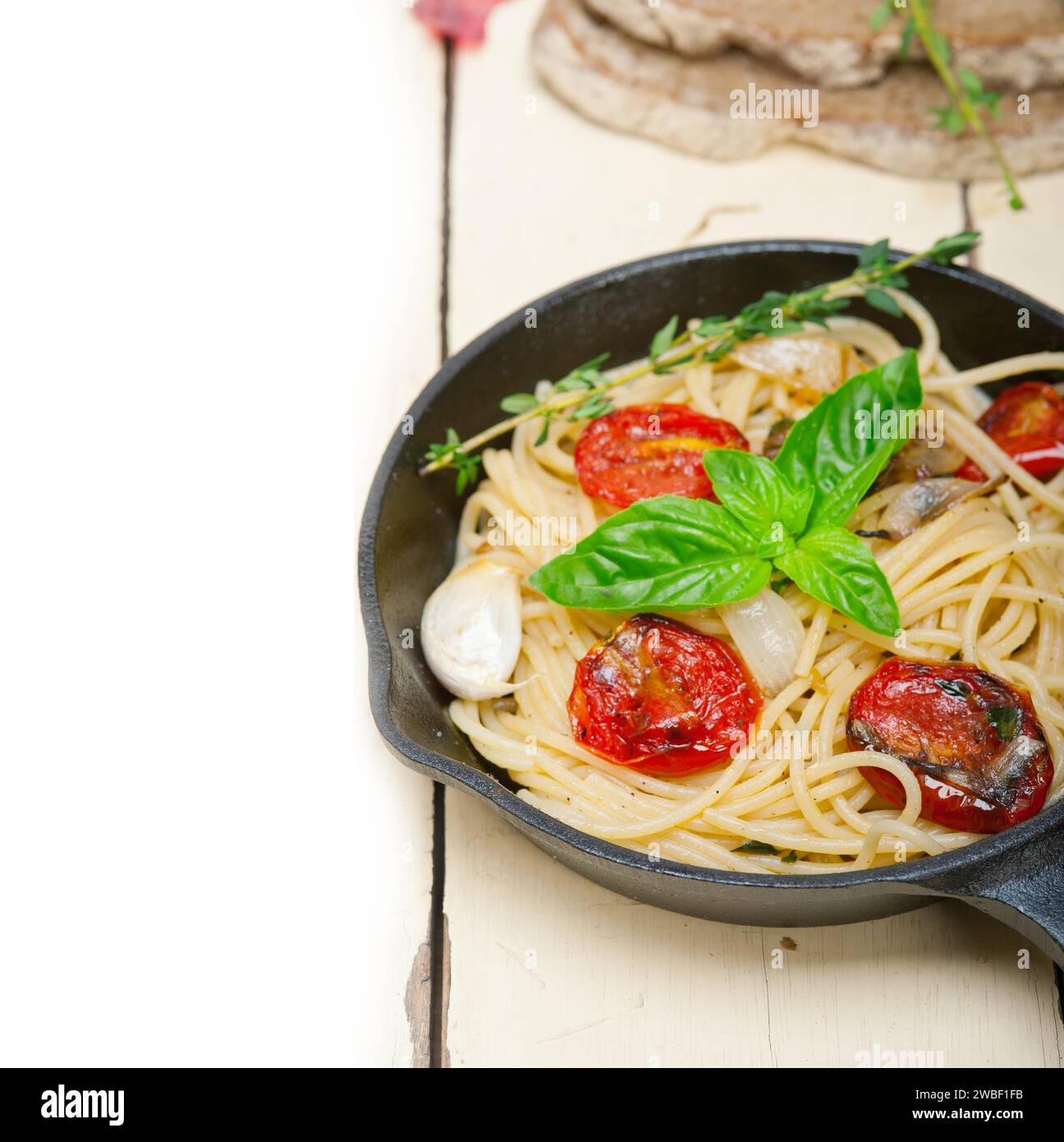 Primo piano degli spaghetti cotti con pomodori ciliegini arrostiti, aglio e basilico fresco Foto Stock