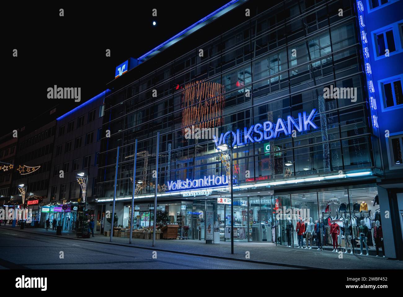 Moderna filiale di banca con facciata in vetro illuminata in una scena urbana notturna, Volksbankhaus, Pforzheim, Germania Foto Stock