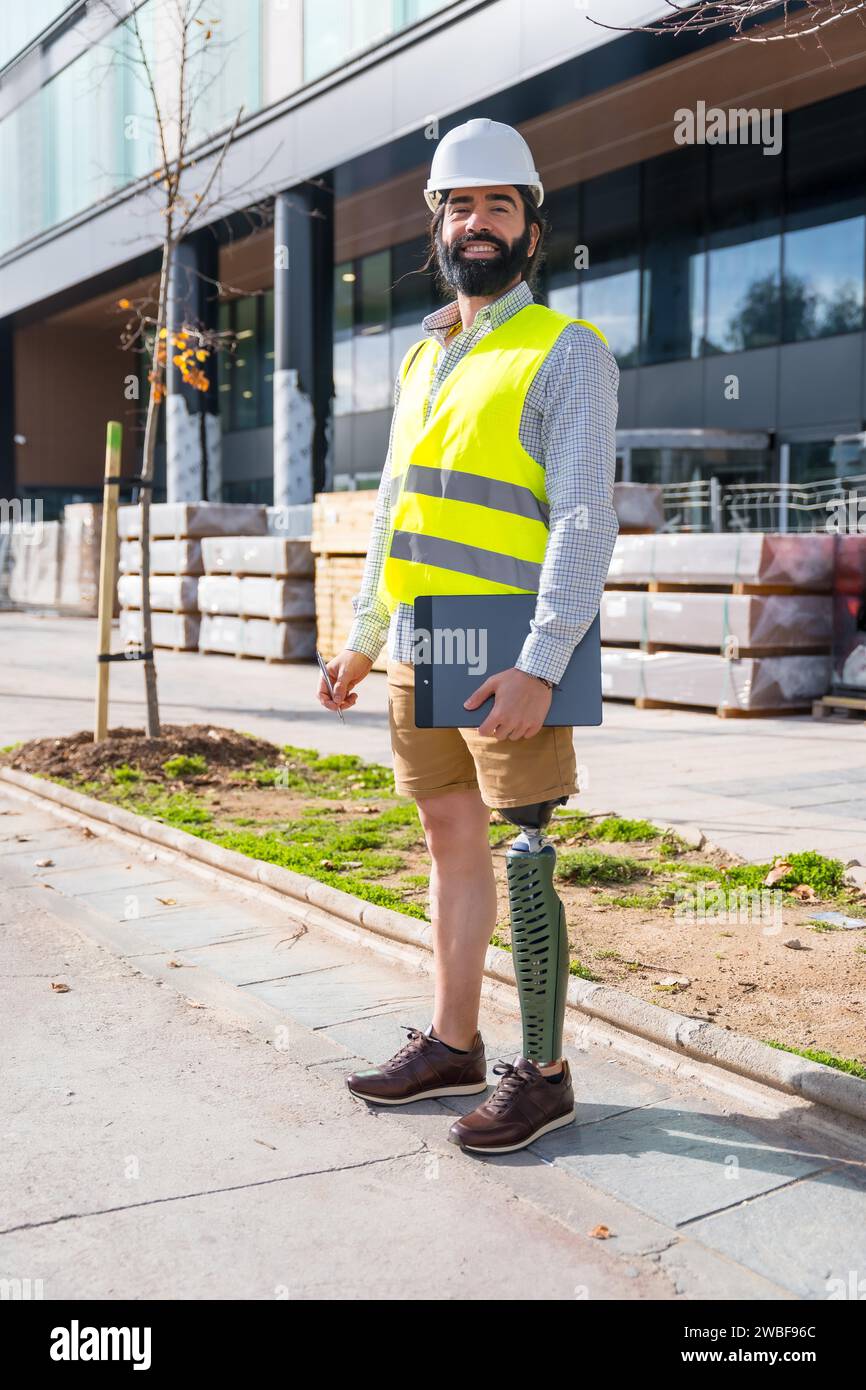 Ritratto verticale di un dipendente con una gamba protesica che lavora in cantiere e indossa dispositivi di protezione Foto Stock