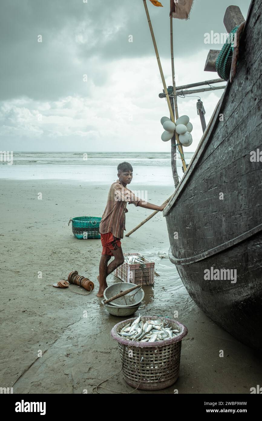 Fisherman sulla sua barca sulla spiaggia con il pescato del giorno durante una doccia monsonica, Cox's Bazar, Bangladesh Foto Stock