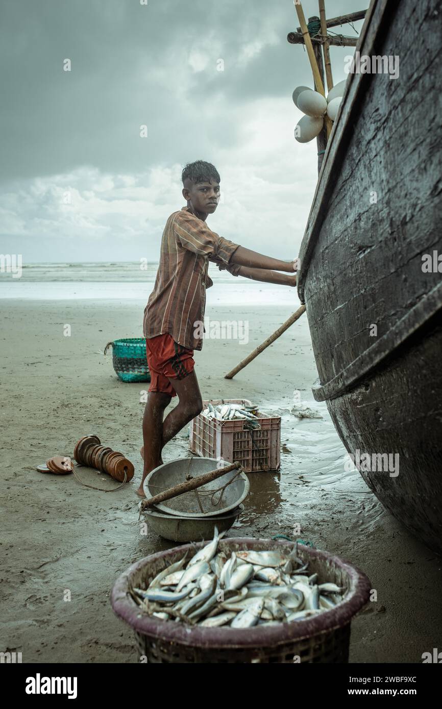 Fisherman sulla sua barca sulla spiaggia con il pescato del giorno durante una doccia monsonica, Cox's Bazar, Bangladesh Foto Stock