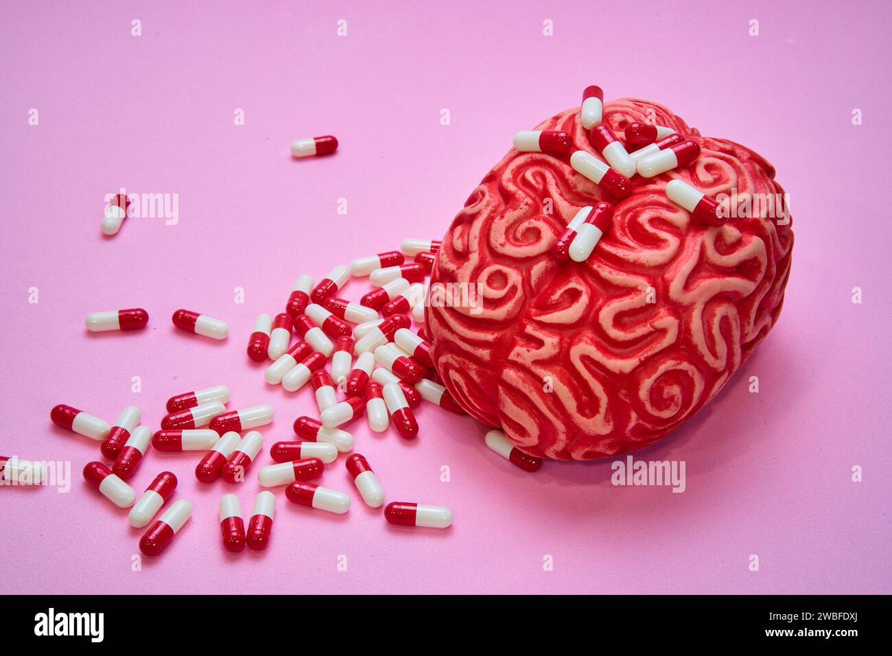 Cervello umano rosso con una pila di pillole e capsule rosse e bianche su un tavolo rosa. Foto Stock