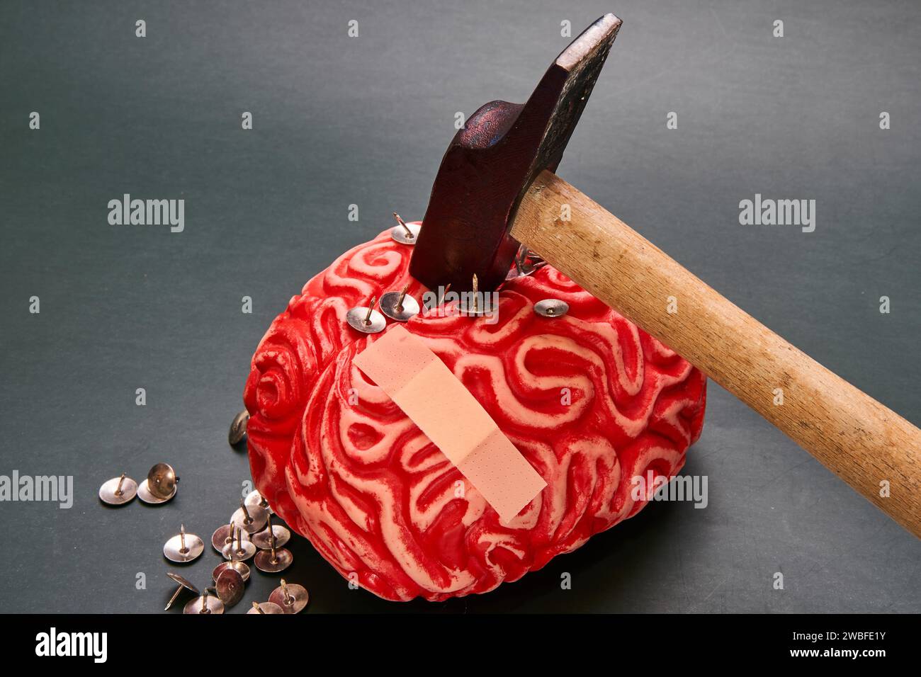 Hammer colpisce il cervello umano rosso pieno di tacche su sfondo scuro. Riparazione cognitiva. Foto Stock