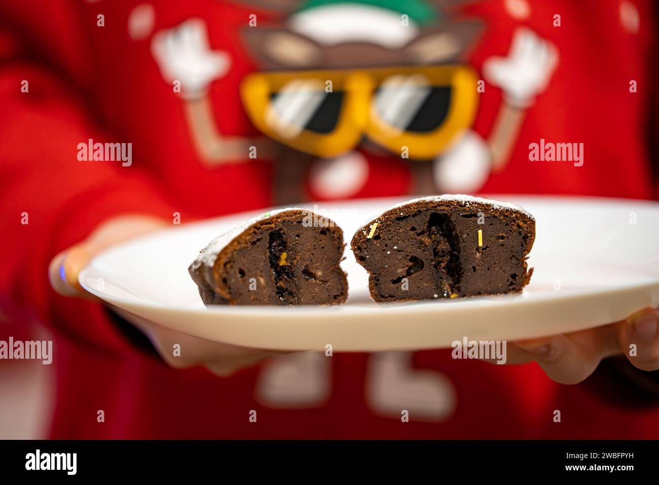 Una persona che indossa una felpa con cappuccio rosso brillante tiene un piatto con una deliziosa torta al cioccolato che è stata parzialmente consumata Foto Stock