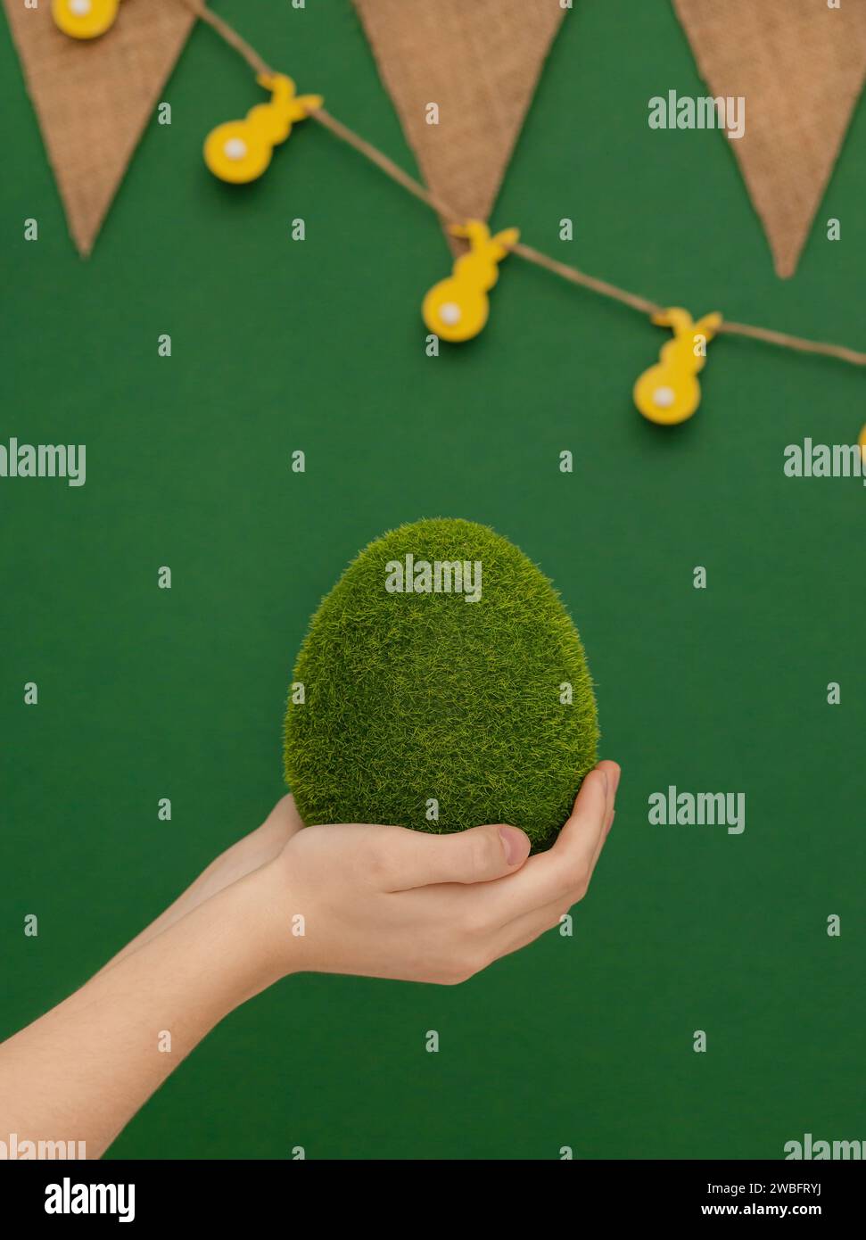 Tema pasquale. Uovo grande, erba, in mani umane su sfondo verde. Uova di Pasqua ecologiche. Foto Stock