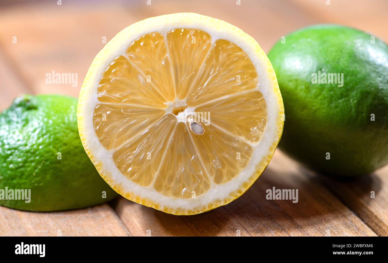 Limone fresco tagliato a metà con limone verde su entrambi i lati, su un tagliere di legno. Foto Stock