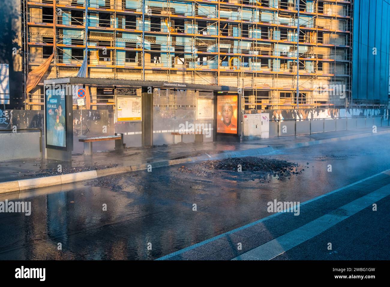 In den frühen Morgenstunden des heutigen Tages ereignete sich an der Haltestelle Hauptbahnhof-Westseite a Lipsia ein Wasserrohrbruch, der vermutlich auf kältebedingte Ursachen zurückzuführen ist. Eine Trinkwasserleitung brach direkt unter dem Wartehäuschen, wodurch das Gehwegpflaster aufbrach und das Wartehäuschen schwer beschädigt wurde. BEI eisigen Temperaturen von -11Â Celsius Floss das Wasser etwa eine Stunde lang die Kurt-Schumacher-Straße hinunter, bis die Leipziger Stadtwerke erfolgreich die Leitung schließen konnten. Die Baustelle des Hotel Astoria wurde ebenfalls a Mitleidenschaft Foto Stock