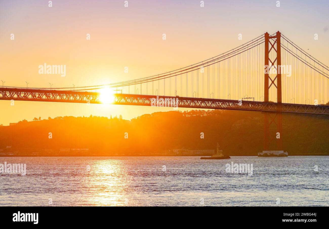 Alba dorata dietro il ponte 25 de Abril a Lisbona, Portogallo, che getta un caldo bagliore sul fiume Tago in un momento di pace e bellezza. Foto Stock