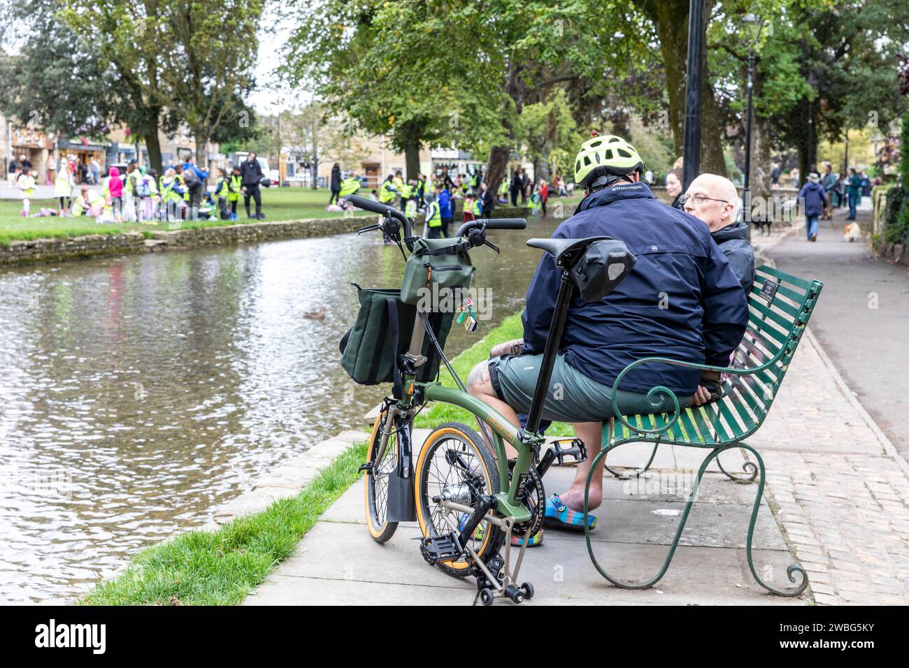 Ciclista maschile a Bourton on the Water con una Brompton x Bear Grylls C Line Esplora la bici pieghevole, divertiti a conversare con un amico, Inghilterra, Regno Unito, 2023 Foto Stock