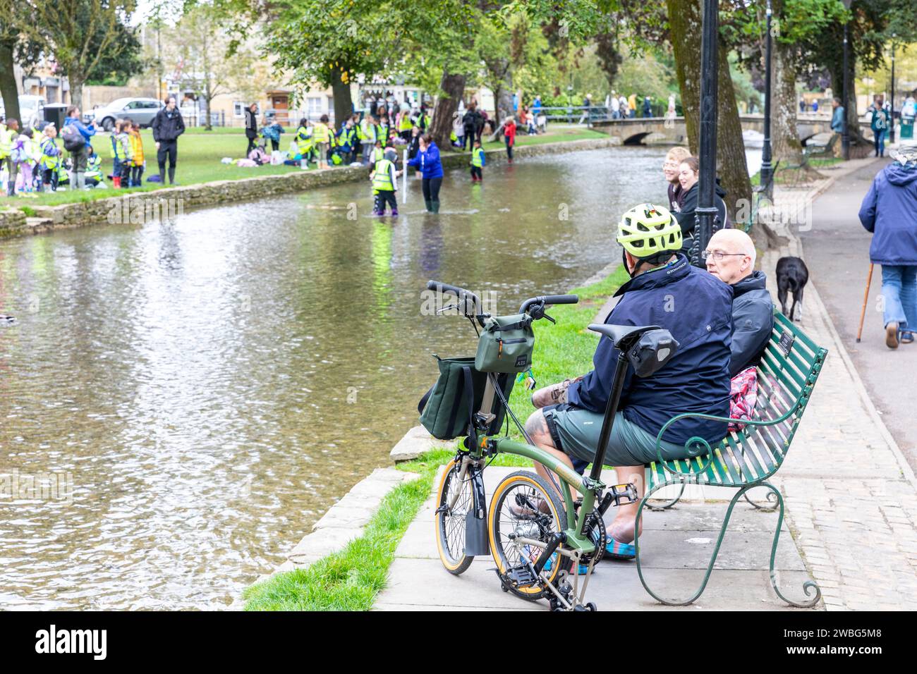 Ciclista maschile a Bourton on the Water con una Brompton x Bear Grylls C Line Esplora la bici pieghevole, divertiti a conversare con un amico, Inghilterra, Regno Unito, 2023 Foto Stock