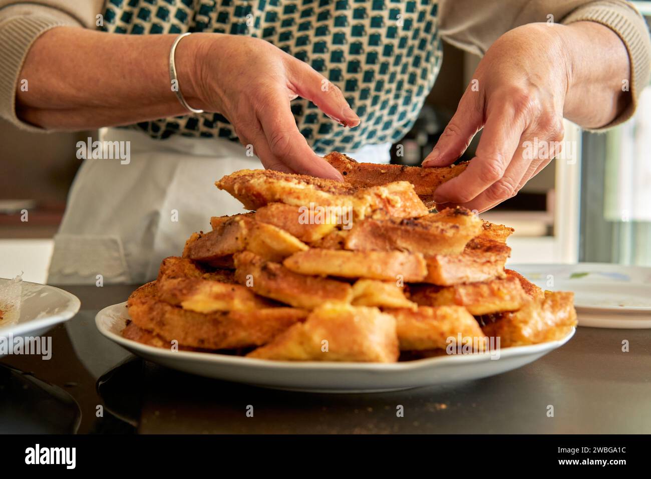 Primo piano delle mani di una donna anziana che posiziona con cura una torrija sulla sommità di una torre di torrija Foto Stock