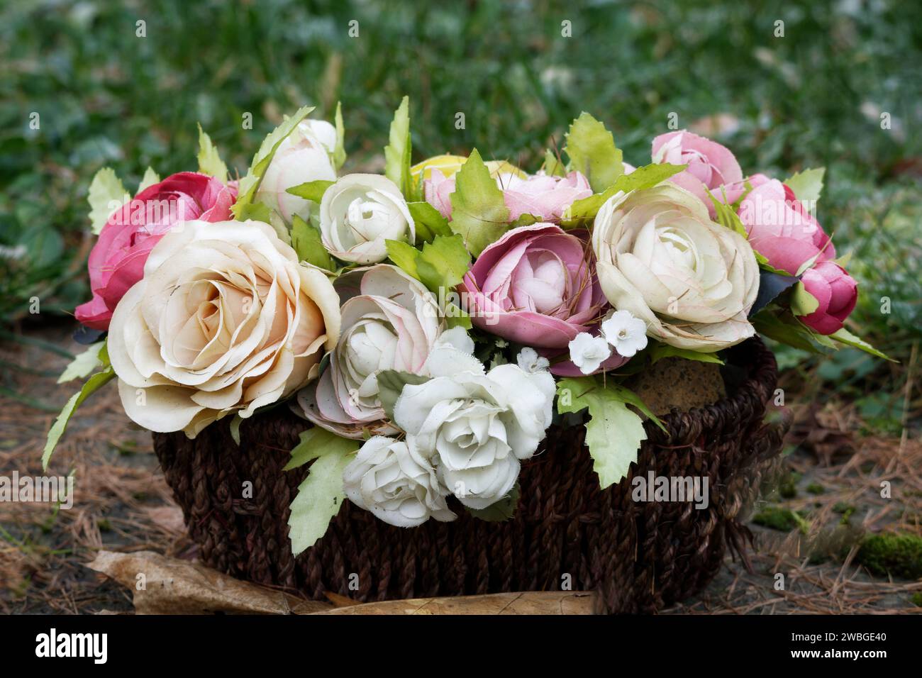 un cesto di rose artificiali sbiadite di colore pastello su una tomba in un cimitero Foto Stock