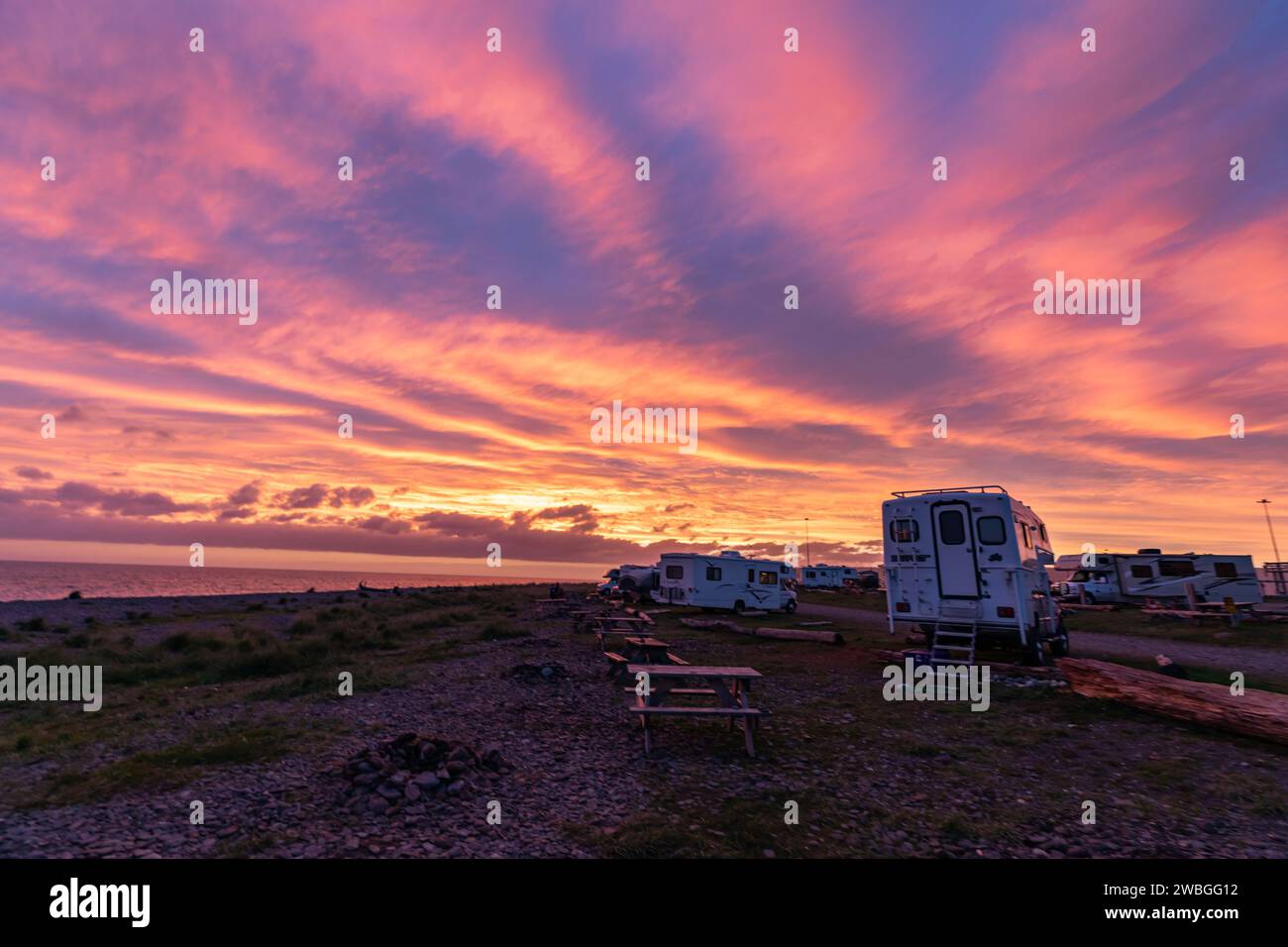 Il tramonto scintillante illumina il cielo con rosa, arance e viola luminosi che dipingono il cielo al tramonto sopra il picnic e i campeggi sul fronte oceano Foto Stock