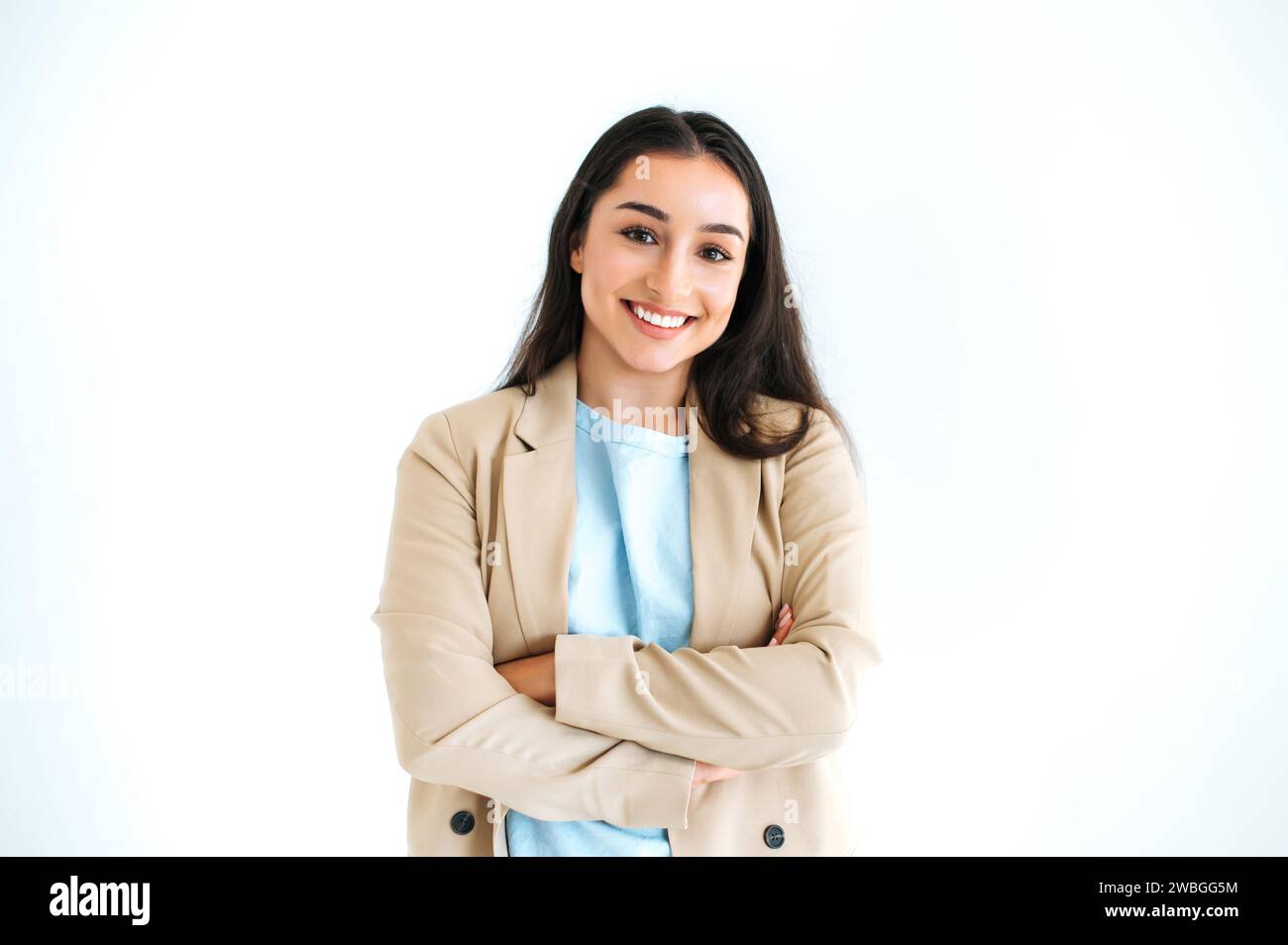Ritratto di una donna d'affari indiana o araba di successo, dirigente, designer, vestita in elegante abito, si erge su uno sfondo bianco isolato con le braccia incrociate, guardando la fotocamera e sorridendo Foto Stock