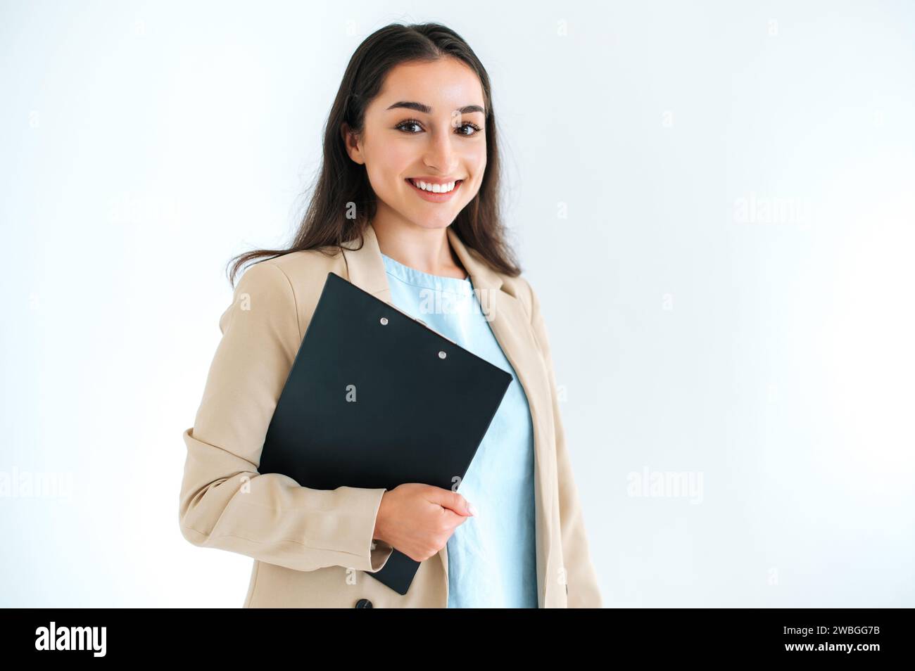 Donna d'affari indiana o araba di successo, consulente finanziario, manager, si trova su uno sfondo bianco isolato, tiene una cartella con i documenti, guarda la fotocamera e sorride Foto Stock