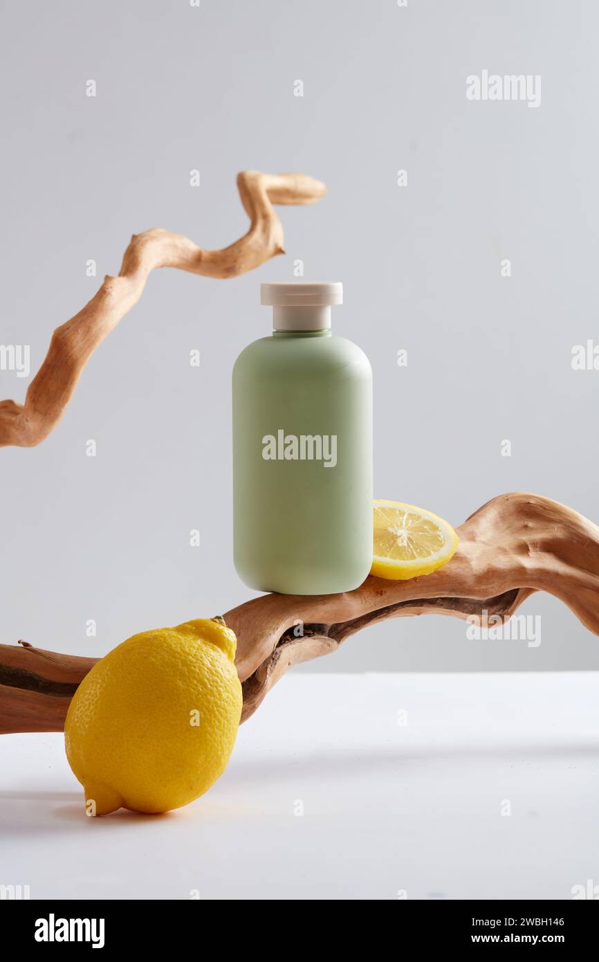 Scena per la pubblicità di prodotti con estratto di limone - limone fresco decorato con bottiglia verde senza etichetta e ramoscelli asciutti su sfondo bianco. I limoni sono ric Foto Stock