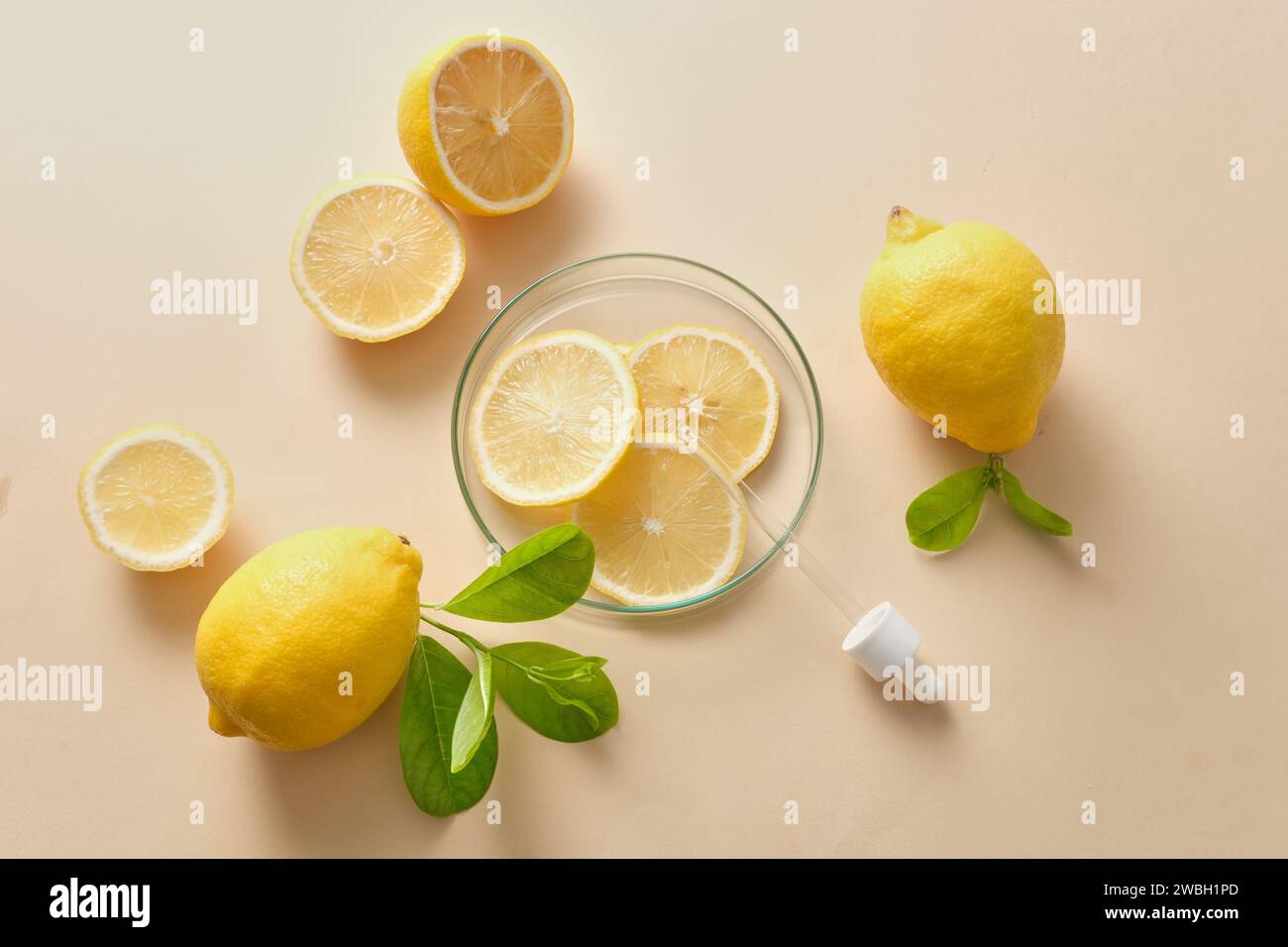 Scena promozionale per cosmetici e prodotti per la cura della pelle con vitamina C naturale - decorazione di limone fresco, fette di lime e foglie verdi su sfondo beige Foto Stock