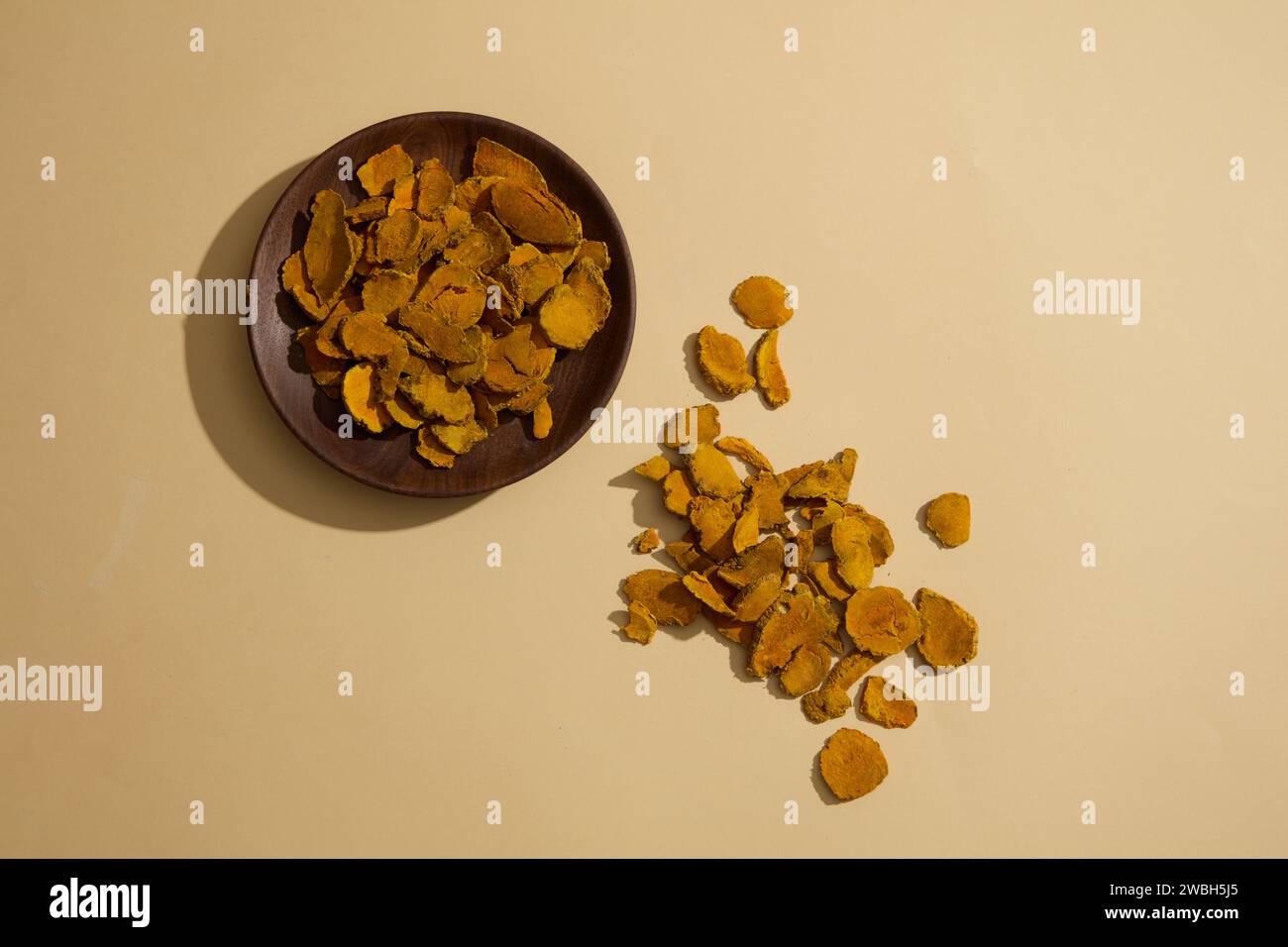 Un piatto di fette di curcuma essiccate visualizzato sulla superficie beige. La curcuma essiccata (Curcuma longa) è una delle spezie ampiamente utilizzate che aggiungono colori sorprendenti e. Foto Stock