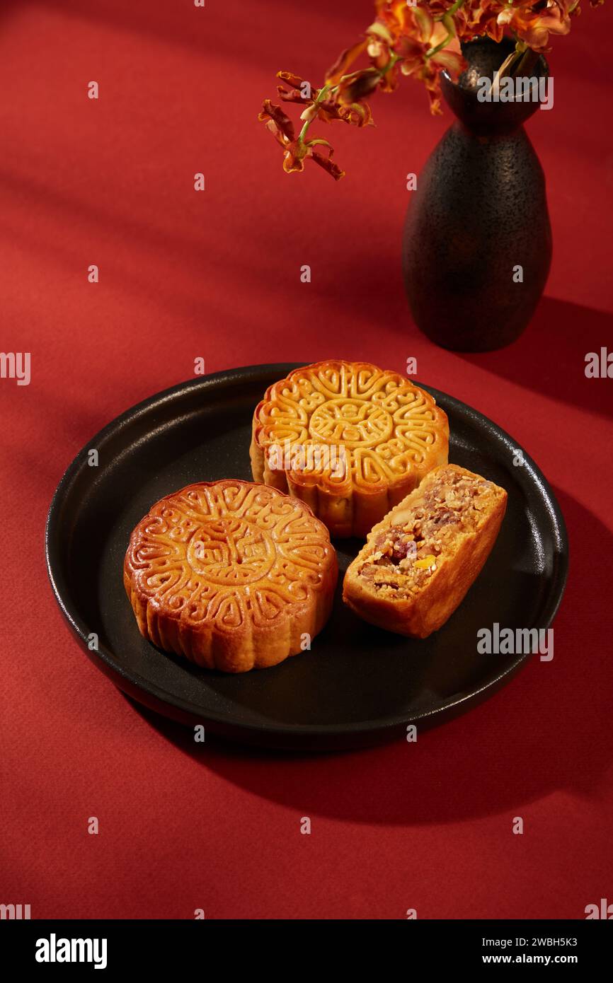 Scena minimalista di un piatto a forma rotonda contenente gustose torte lunari. Sfondo rosso per la pubblicità. Mooncake festival di metà autunno in stile minimalista Foto Stock