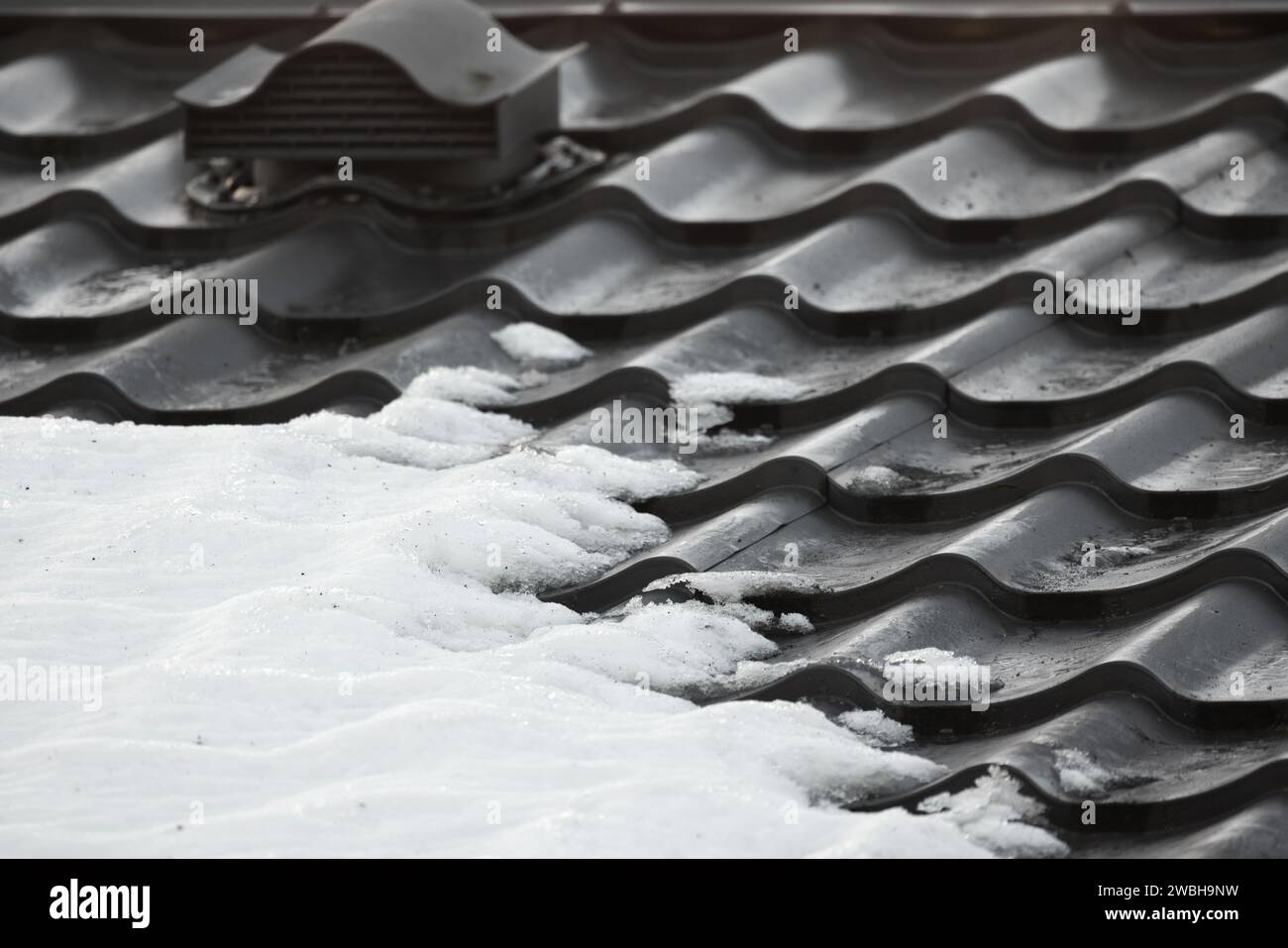 Tetto in metallo nero con piastrelle di neve, foto invernale ravvicinata del tetto di una moderna casa di campagna Foto Stock