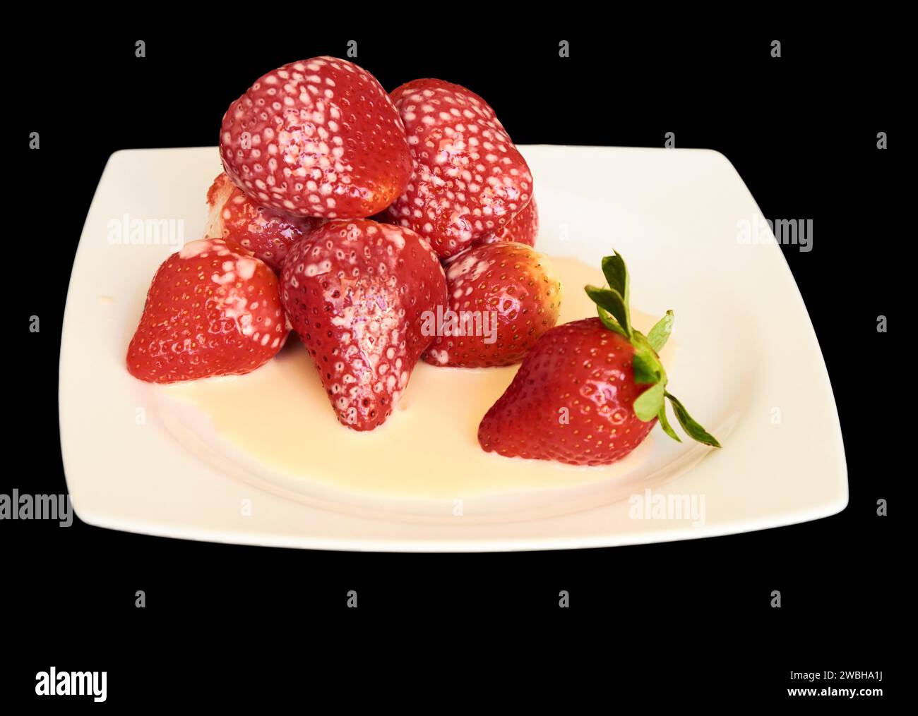 Fragole mature ricoperte di yogurt su un piatto quadrato bianco su uno sfondo nero isolato Foto Stock