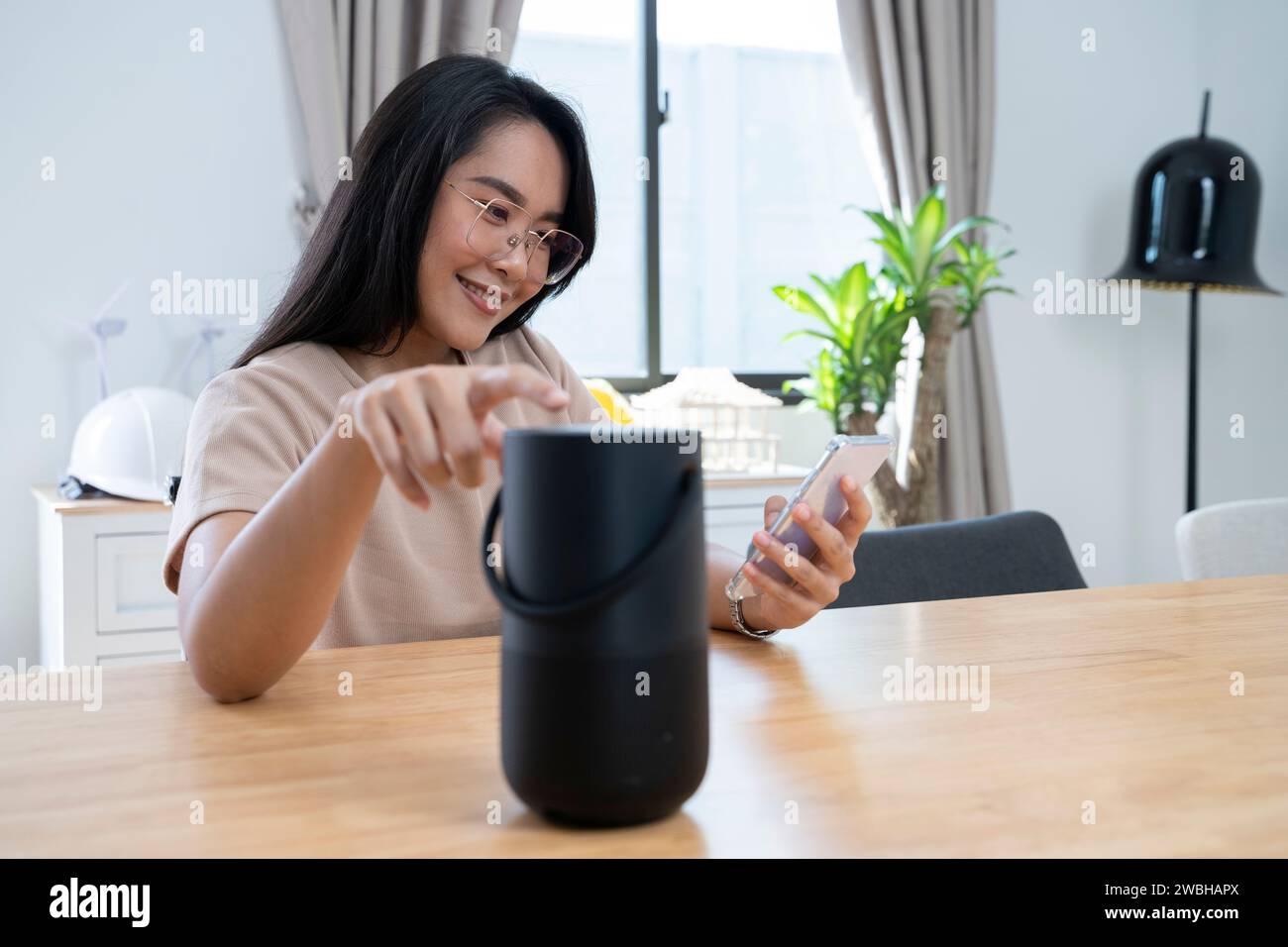 Giovane donna asiatica lavora da casa con un altoparlante intelligente per assistenza. Foto Stock