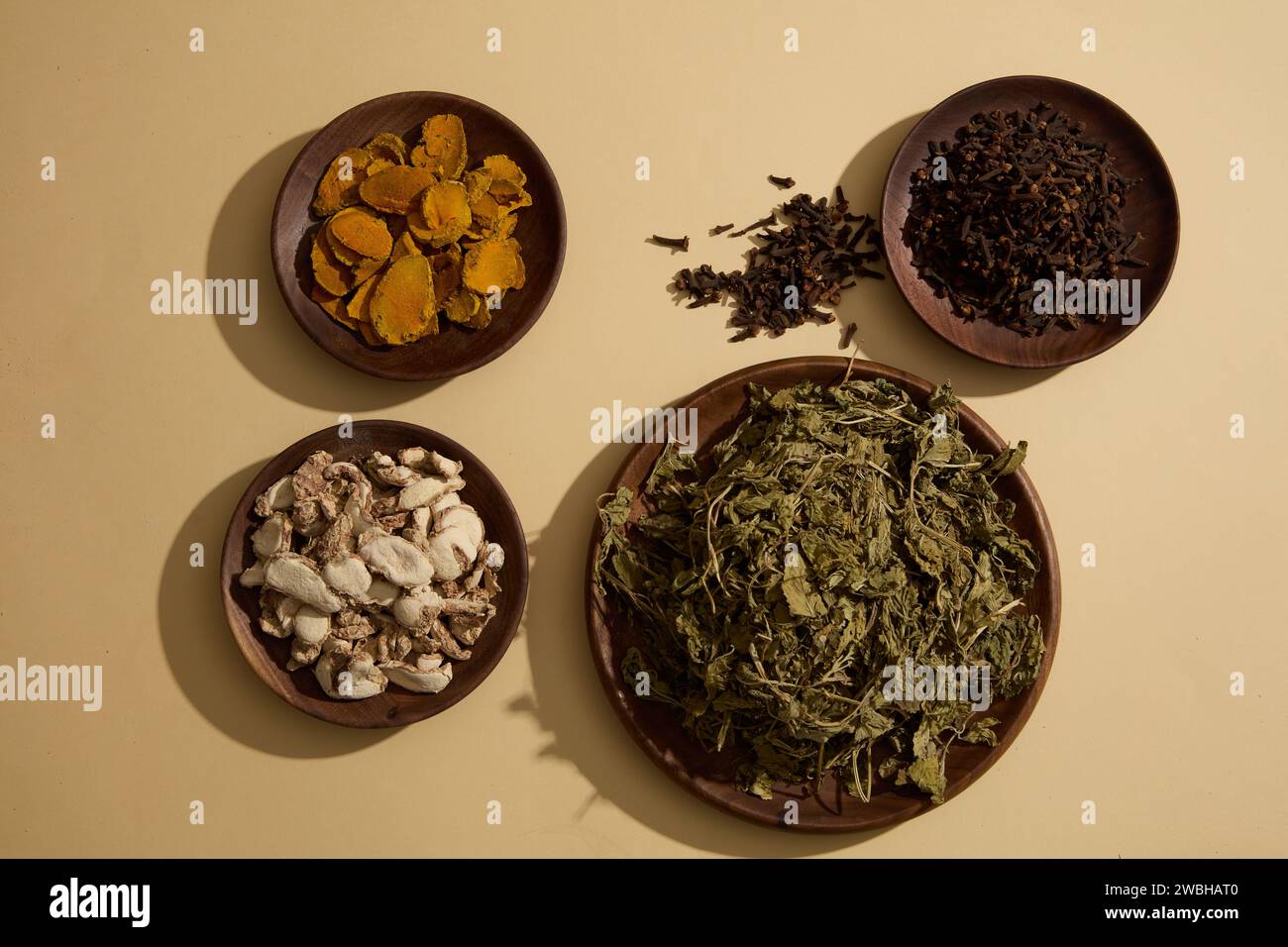 Lo zenzero aromatico, la curcuma essiccata, i chiodi di garofano e le foglie di menta secche sono decorate su piatti rotondi di legno su sfondo beige. Concetto di medicina sana Foto Stock