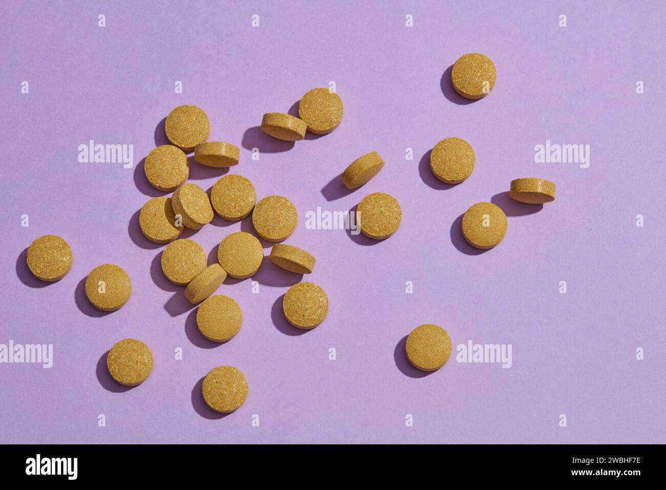 Vista dall'alto, piatto di molte pillole rotonde verdi su sfondo di carta viola. Scena minimalista con tema medico per la pubblicità. Foto Stock