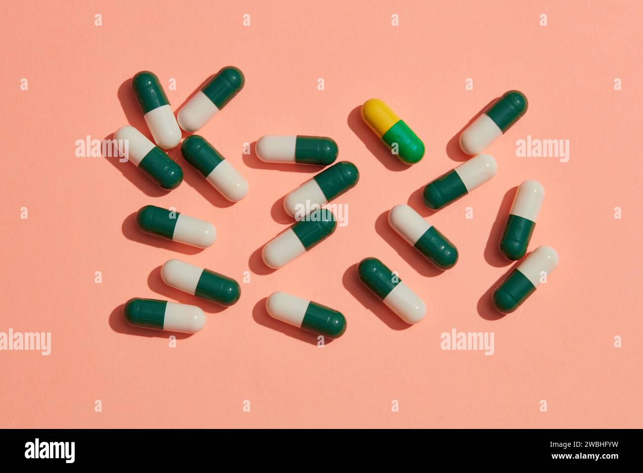 Una pillola di capsula gialla mescolata con le pillole di capsule bianche e verdi su sfondo rosa. Tema farmacia, Close Up creativo farmacia o assistenza sanitaria Foto Stock