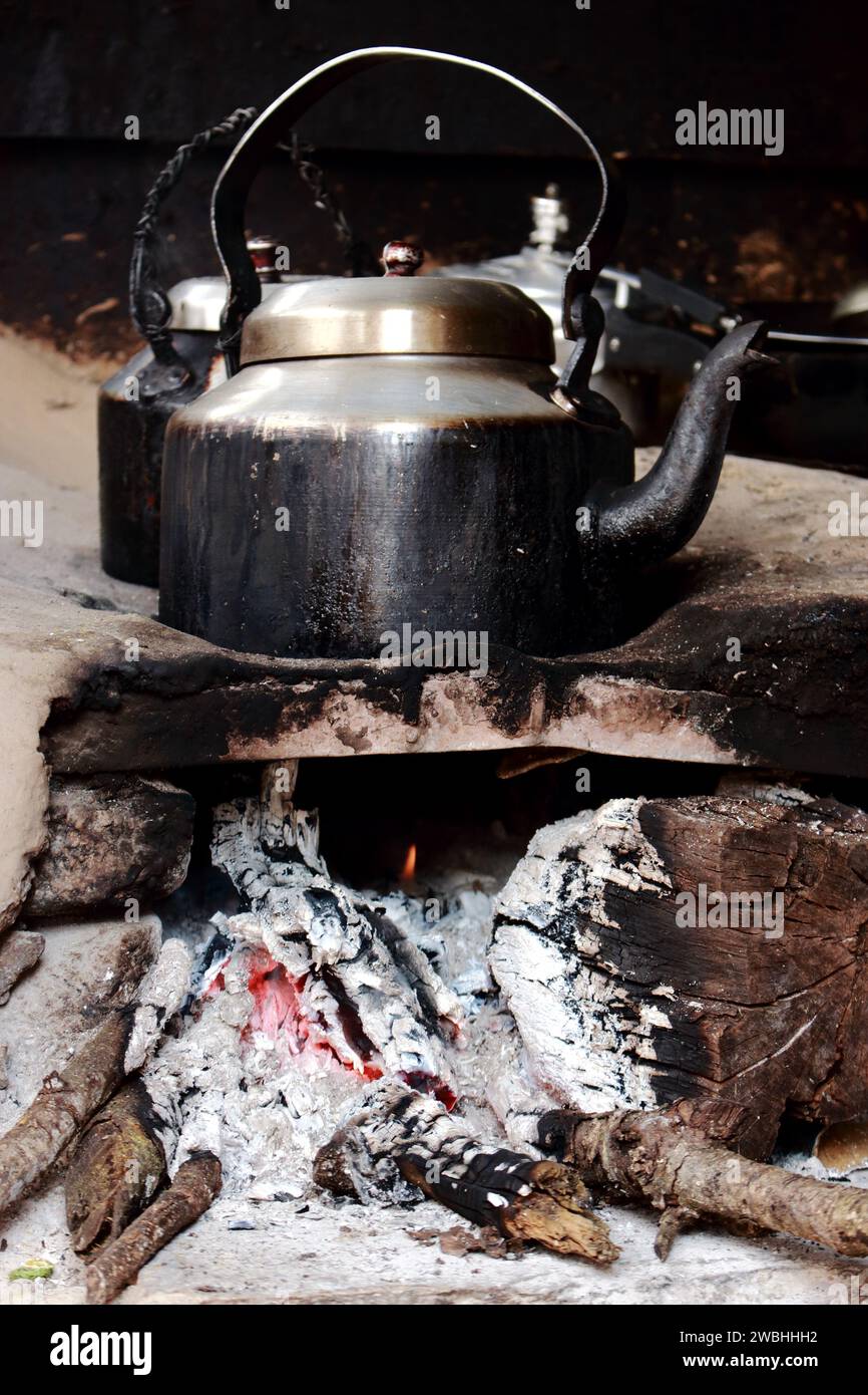 Un vecchio recipiente di metallo affumicato su un caminetto di legno mentre cucinava il tè indiano. Fuoco e utensili da cucina indiani. Cucina all'aperto. Foto Stock
