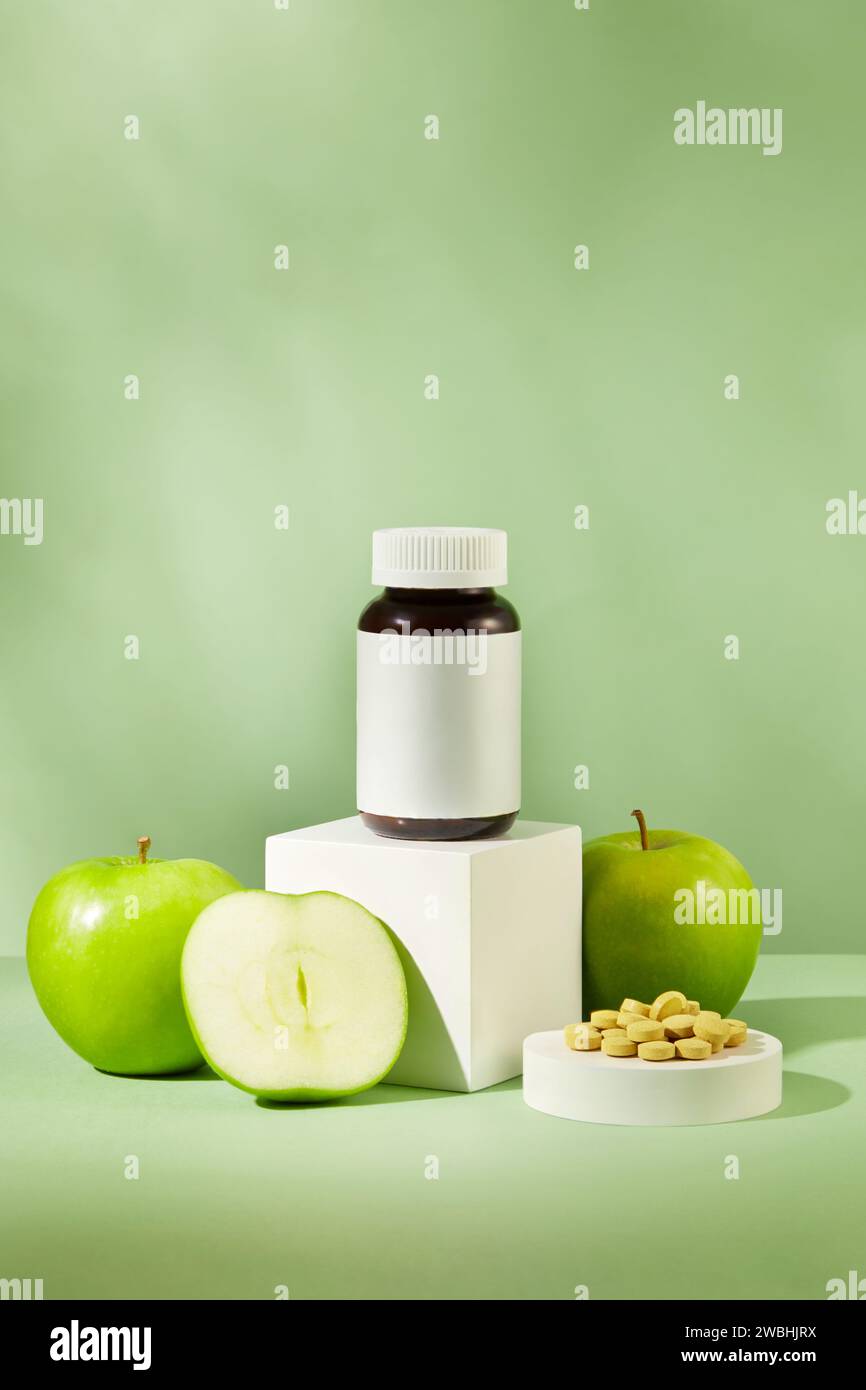 Bottiglia di medicina in piedi su podio bianco con mela verde circondata. Alcune pillole sono sistemate. Medicina, trattamenti e assistenza sanitaria con Mela Verde (M Foto Stock