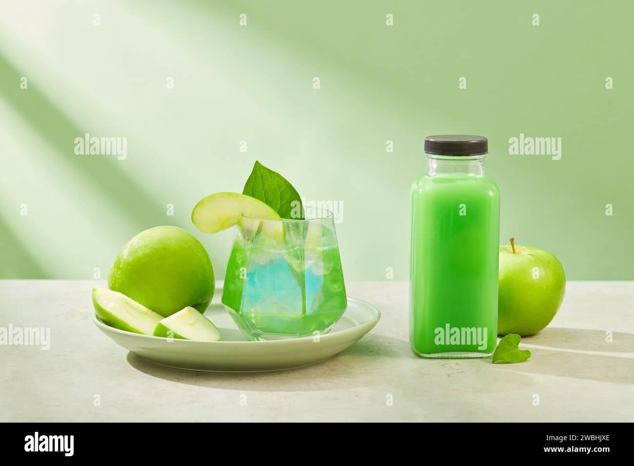 Un lussuoso bicchiere di succo esposto su un piatto con poche fette di mela verde. Bottiglia senza marchio. Green Apple (Malus domestica) è anche buono per Foto Stock