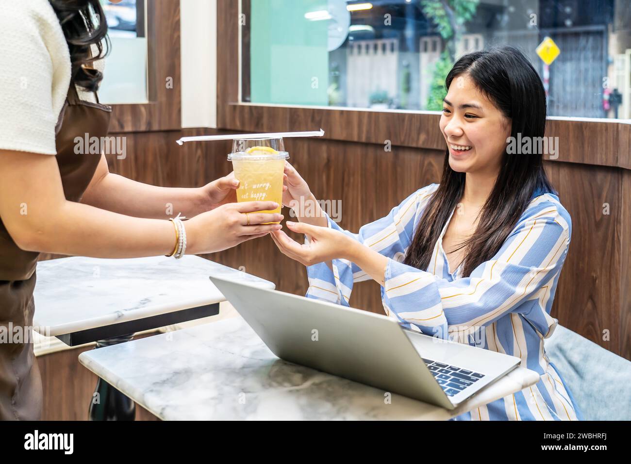 Cameriere che serve un bicchiere di succo di frutta fresco al cliente che era una giovane donna asiatica al tavolo del ristorante, mentre i dipendenti del juice bar servono bevande al cliente Foto Stock