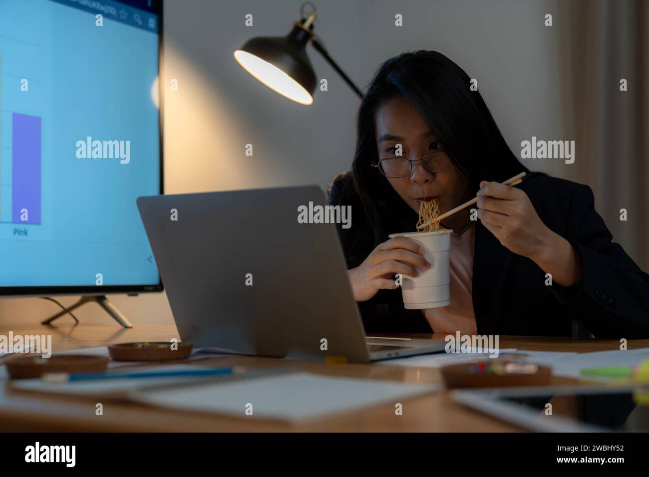 Una donna d'affari che lavora fino a notte fonda e mangia noodles istantanei Foto Stock