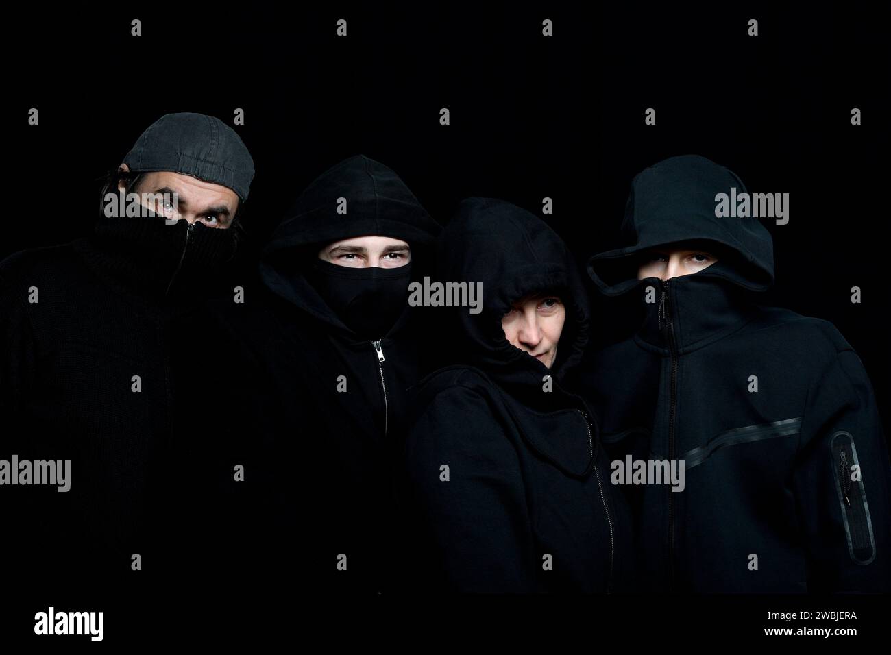 foto in studio di quattro persone che indossano abiti neri con volti nascosti sullo sfondo nero Foto Stock