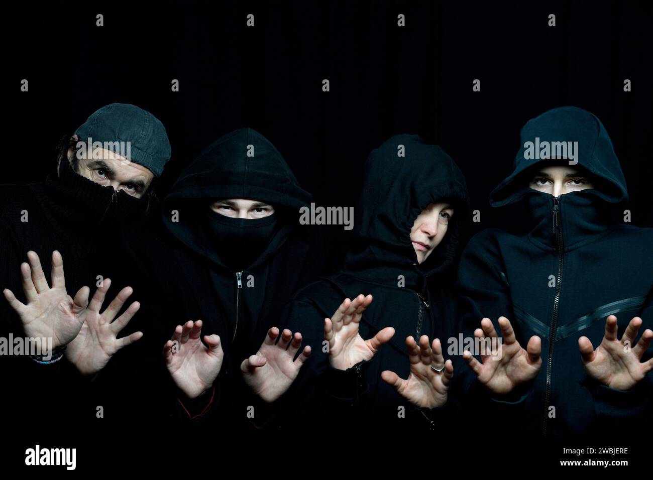 foto in studio di quattro persone che indossano abiti neri con volti nascosti sullo sfondo nero che tengono i palmi in alto Foto Stock