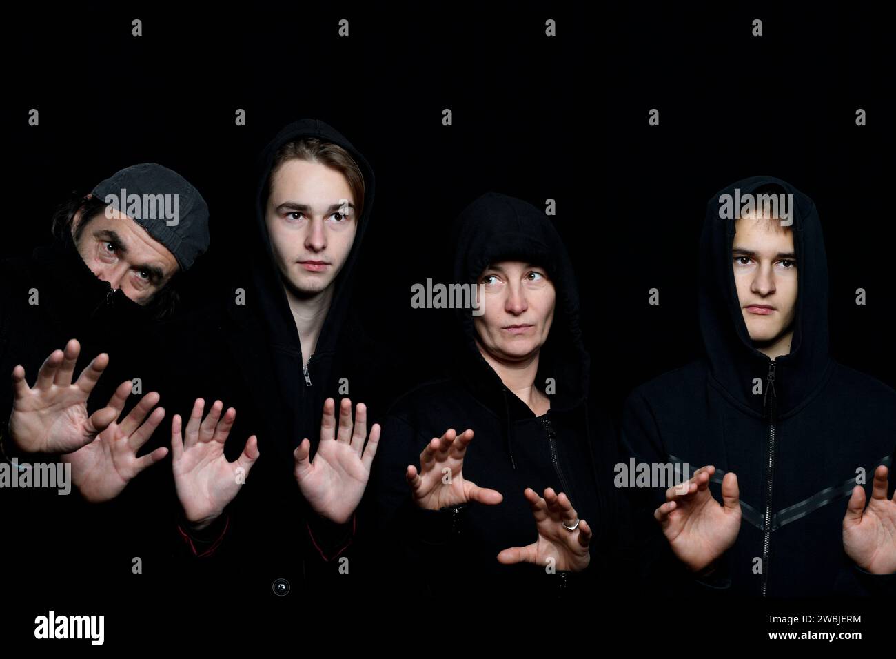 foto in studio di quattro persone che indossano abiti neri sullo sfondo nero tenendo i palmi in alto Foto Stock
