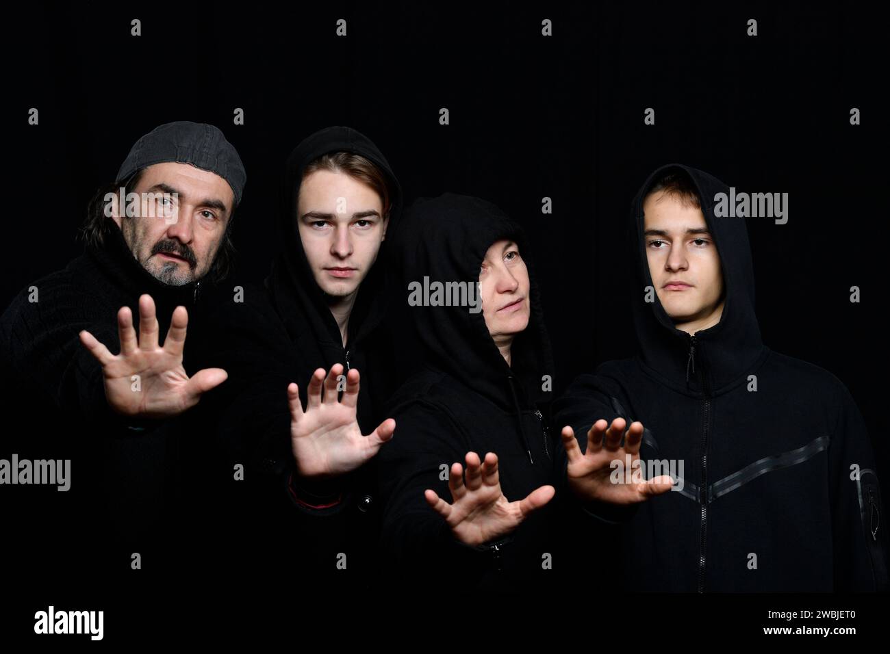 foto in studio di quattro persone che indossano abiti neri sullo sfondo nero tenendo i palmi in alto Foto Stock