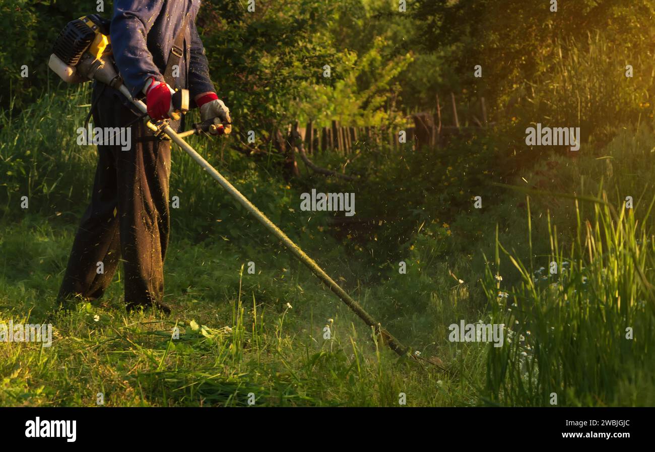 Il giardiniere taglia l'erba in giardino con un rasaerba a gas in mano. Concetto di giardinaggio. Foto Stock