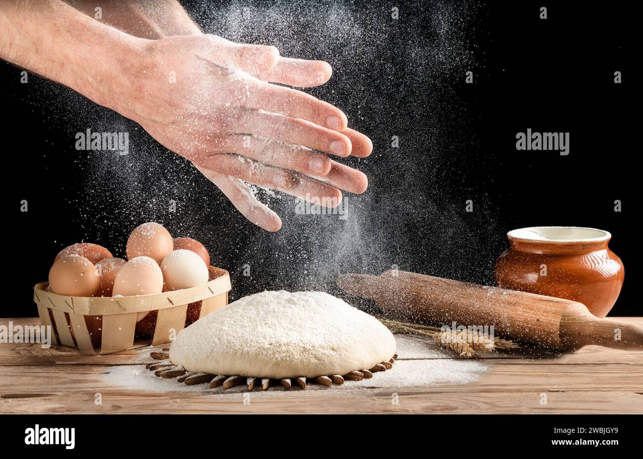 Il fornaio batte le mani con la farina sull'impasto. Un uomo sta preparando del pane fatto in casa in cucina. Cibo sano. Foto Stock