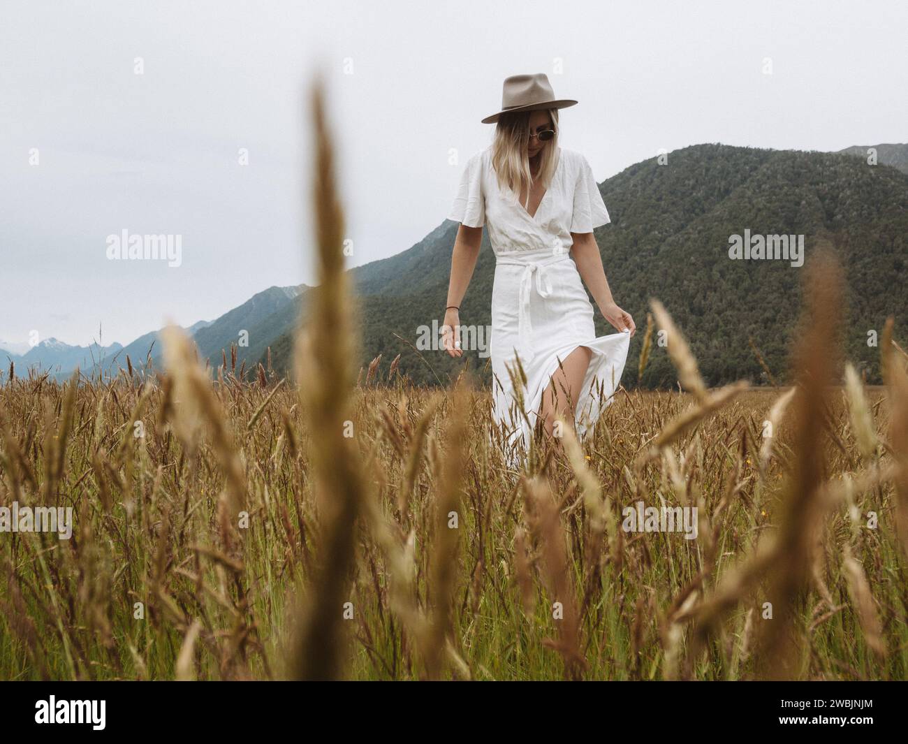 Un'immagine di una ragazza con un abito e un cappello bianco, passeggiando nel sereno prato sulla strada per Milford Sounds, nella splendida nuova Zelanda. Foto Stock