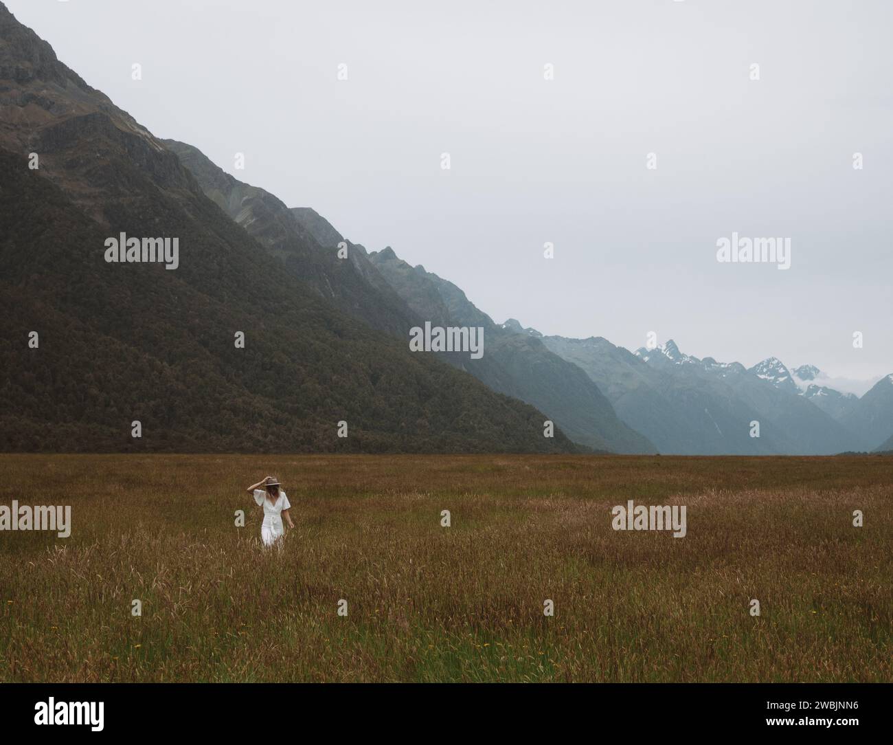 Un'immagine di una ragazza con un abito e un cappello bianco, passeggiando nel sereno prato sulla strada per Milford Sounds, nella splendida nuova Zelanda. Foto Stock